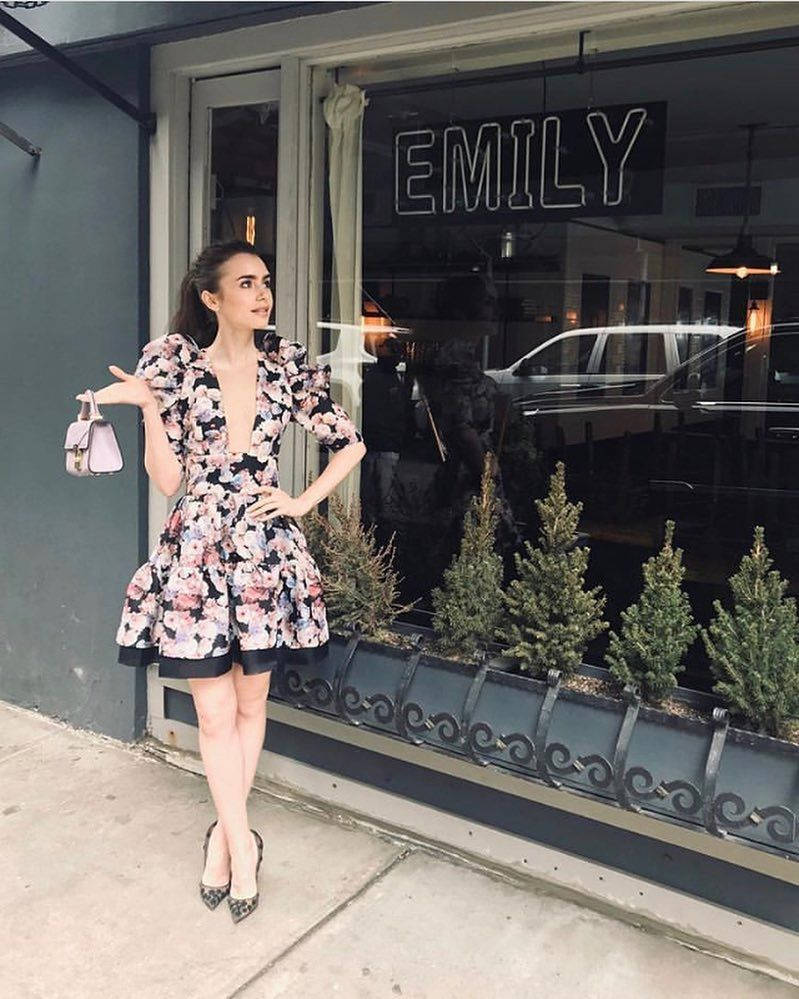 花卉連衣裙女性在 Emily 商店外與常綠植物和汽車反射擺姿勢。