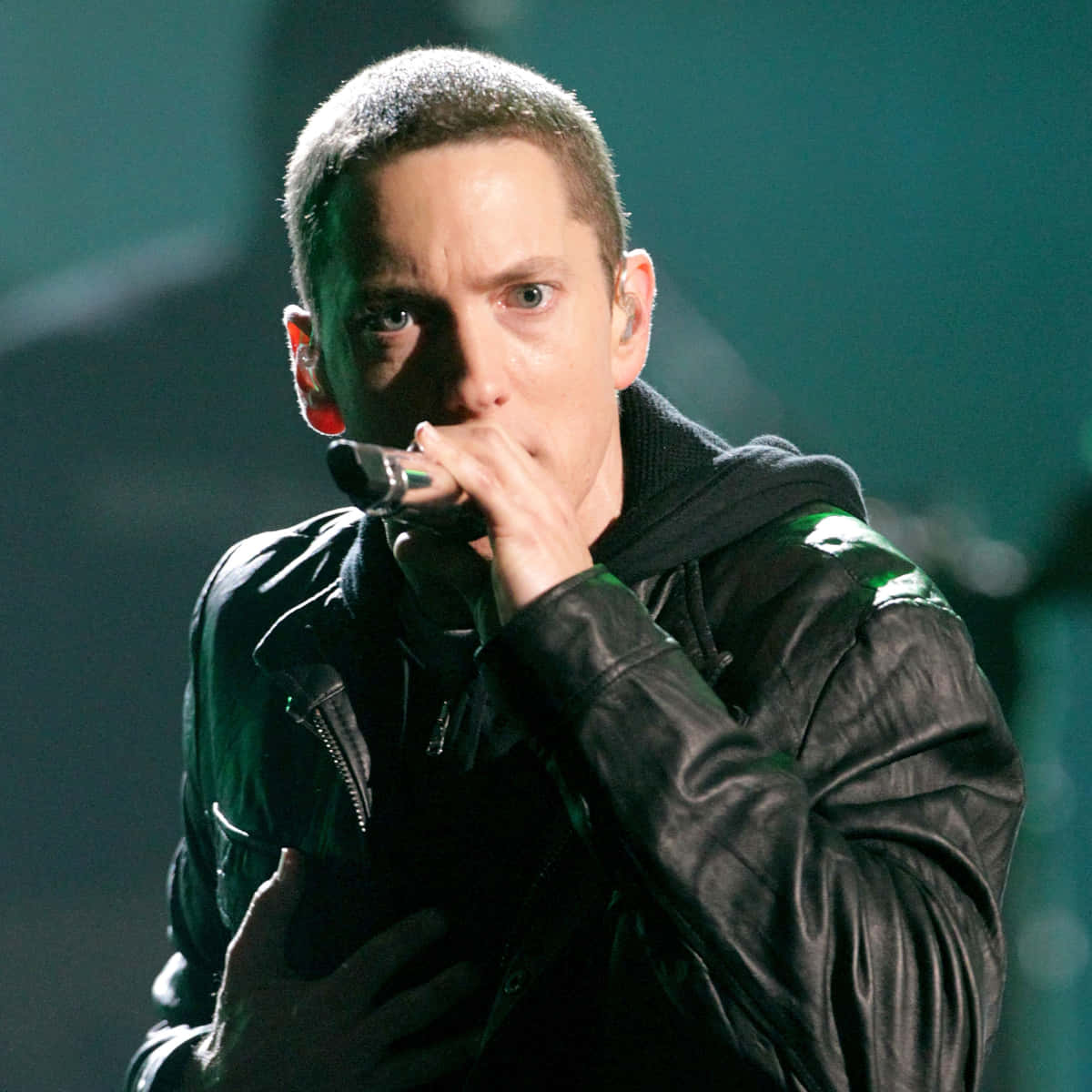 Eminem 桌布 壁紙 — Eminem 在綠色舞台燈光下穿著黑色皮夾克在舞台上表演的特寫。