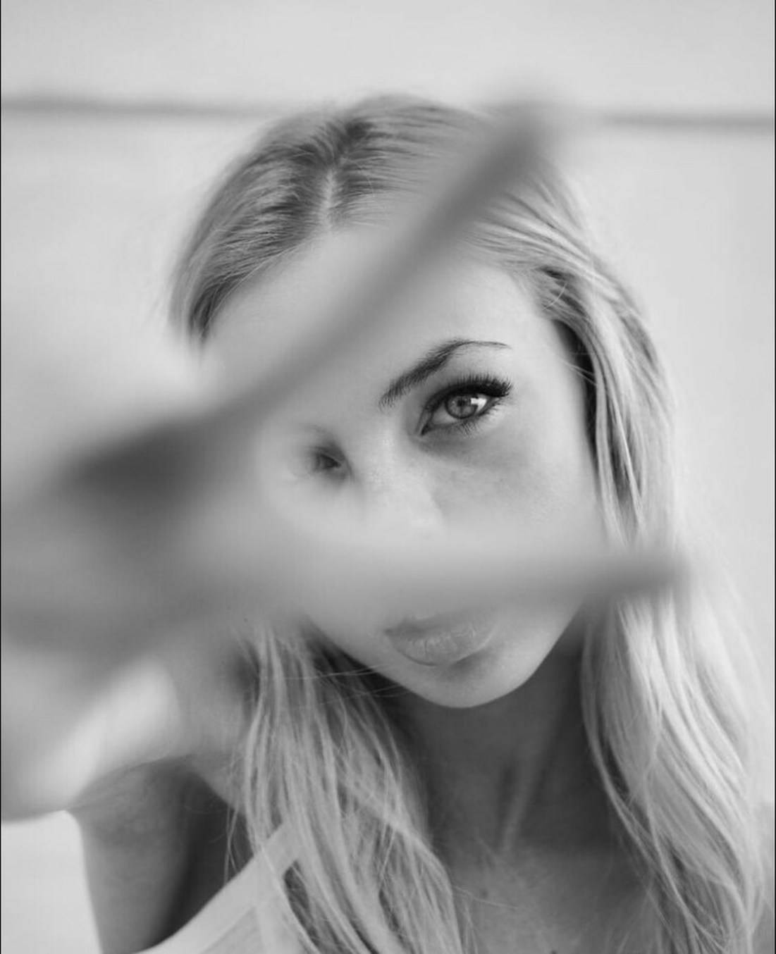 一位金髮女性在黑白肖像中透過模糊前景元素凝視。