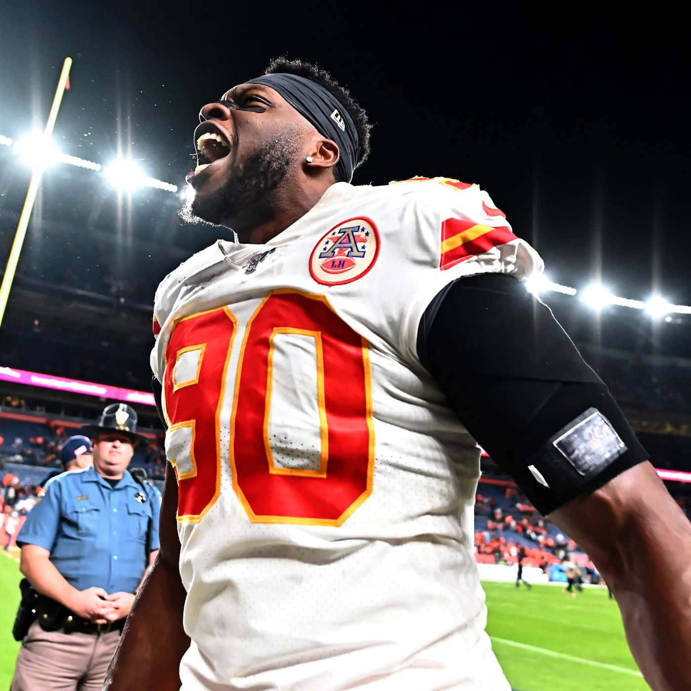 Emmanuel Ogbah 克里夫蘭布朗隊美式足球員 壁紙 — 一名身穿白色球衣、紅色90號的足球運動員在夜間球場燈光下勝利咆哮。