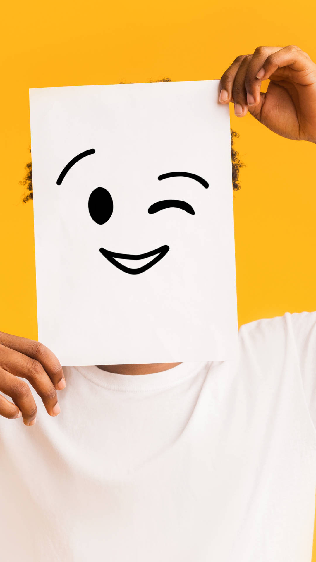 眨眼男子Emoji 壁紙 — 一個人拿著一張白色紙，上面有一個眨眼笑臉，背景是鮮黃色。