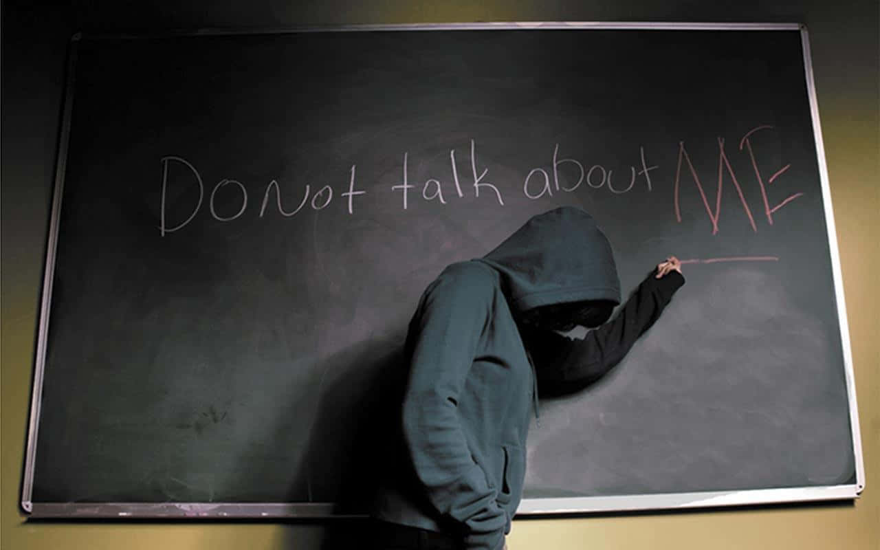 一個穿連帽衫的人正在黑板上寫「Do not talk about ME」。