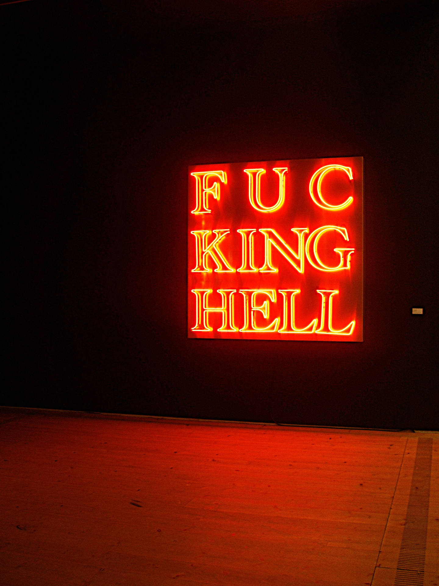 一個在黑暗畫廊空間中寫著「FUCKING HELL」的紅色霓虹藝術品。