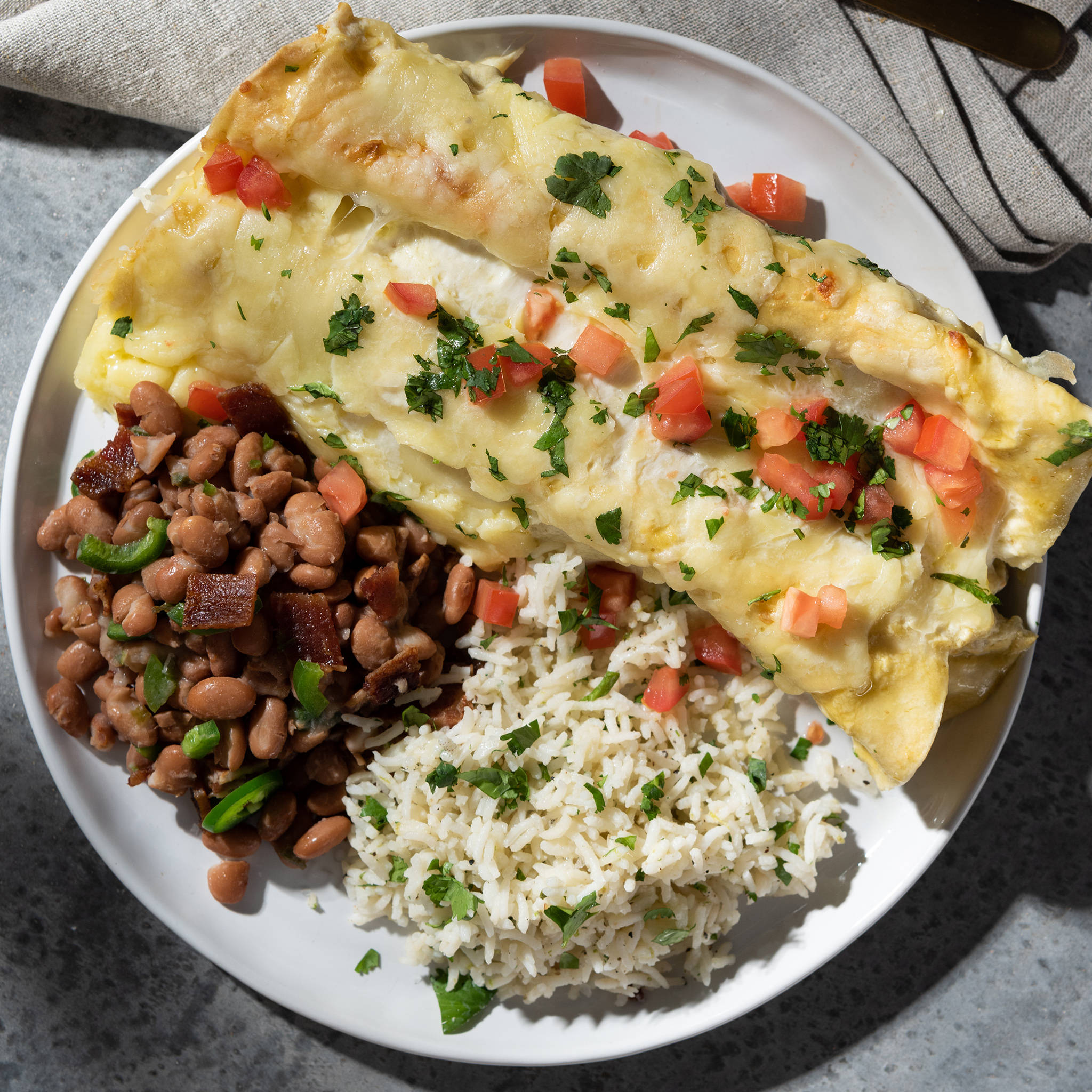 enchiladas 配豆子與飯 壁紙 — 金黃芝士玉米捲餅配上新鮮番茄和芫荽，旁邊有米飯和豆類，放在白色碟子上。