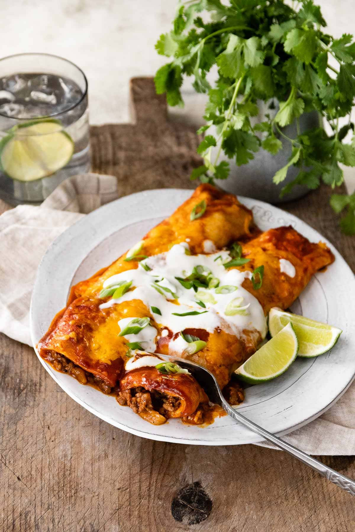 enchiladas 配酸奶油與青檸 壁紙 — 兩塊芝士墨西哥捲餅，上面放有酸忌廉和芫荽，放在一個鄉村風格的碟子上，旁邊有青檸角和一杯水。