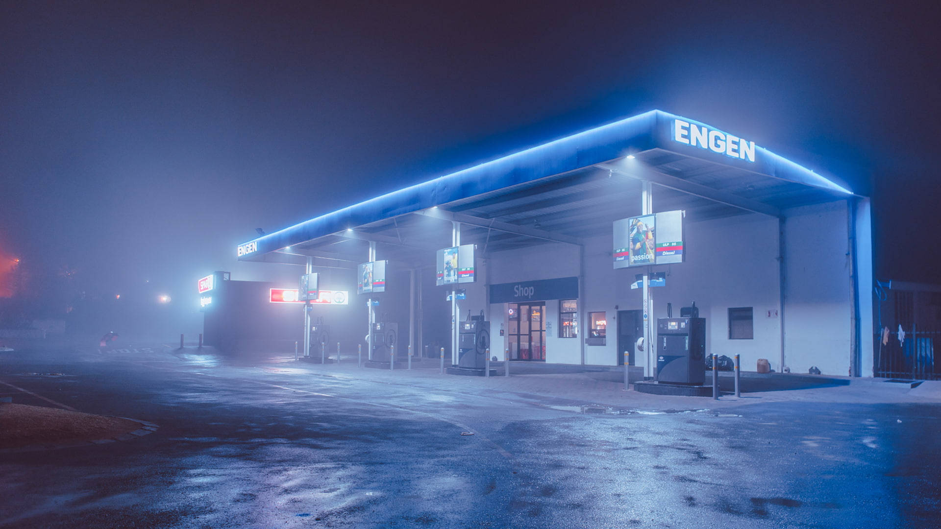 Engen加油站 壁紙 — 一個霧夜，英根加油站發出藍色霓虹燈光，映照在濕漉漉的路面上。