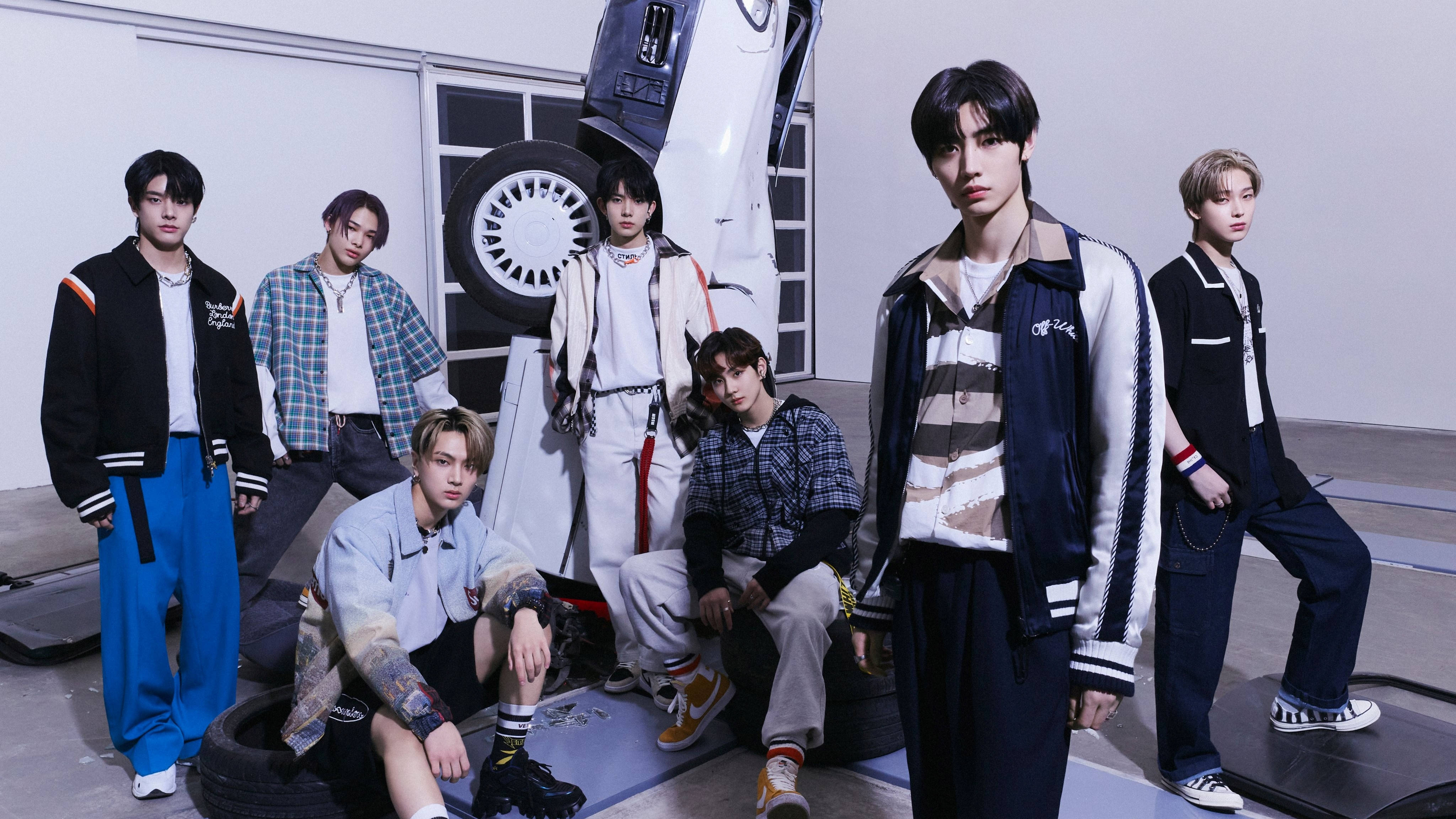 Enhypen《Border: Carnival》Down版造型 壁紙 — 七位時尚年輕男子在簡約工業車庫中自信地圍著一輛翻轉的白色汽車擺姿勢。