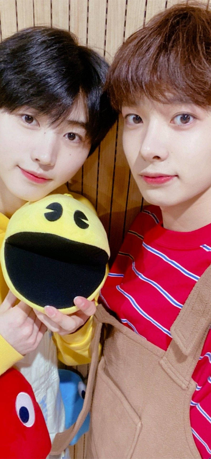 兩名年輕男子在木牆前手持 Pac-Man 毛絨玩具。