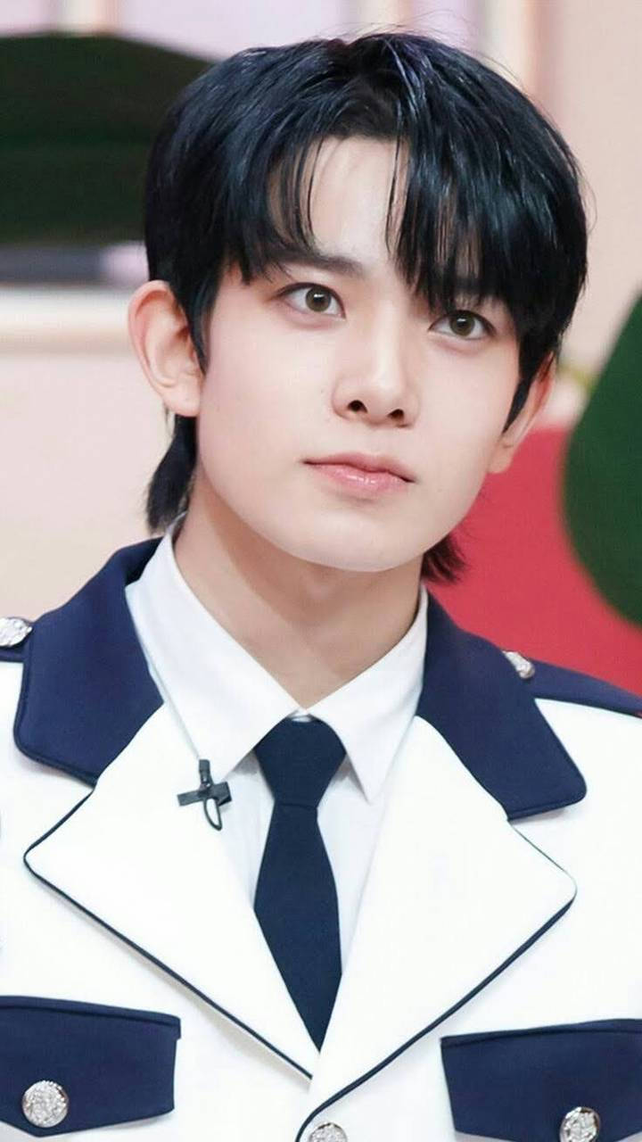 年輕男子穿著正式白色和海軍藍色制服，打黑色領帶，直視鏡頭。