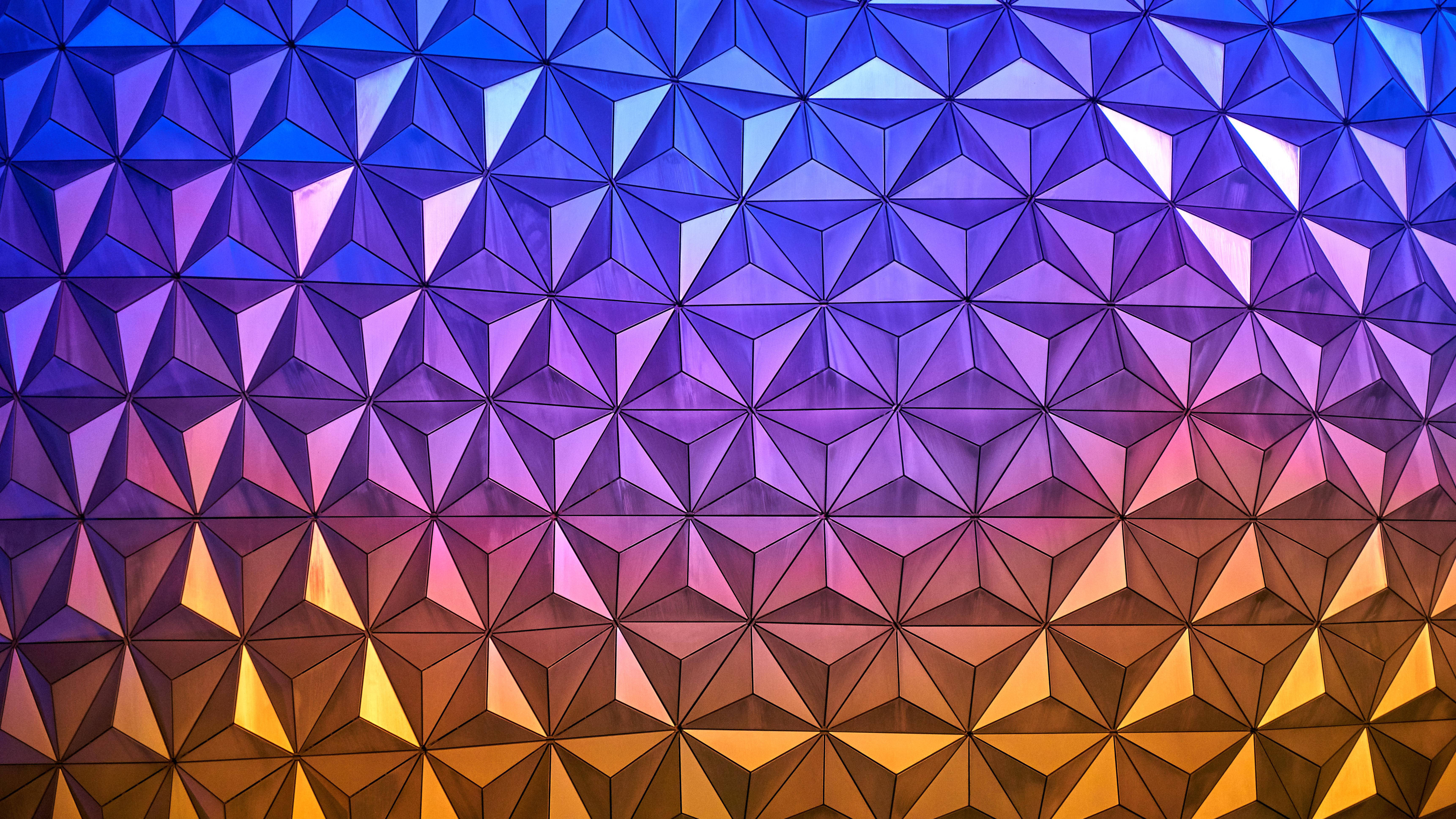 色彩繽紛Epcot地球儀特寫 壁紙 — 充滿活力的幾何牆，帶有三角形切面，從深藍色過渡到暖金色，形成漸變圖案。