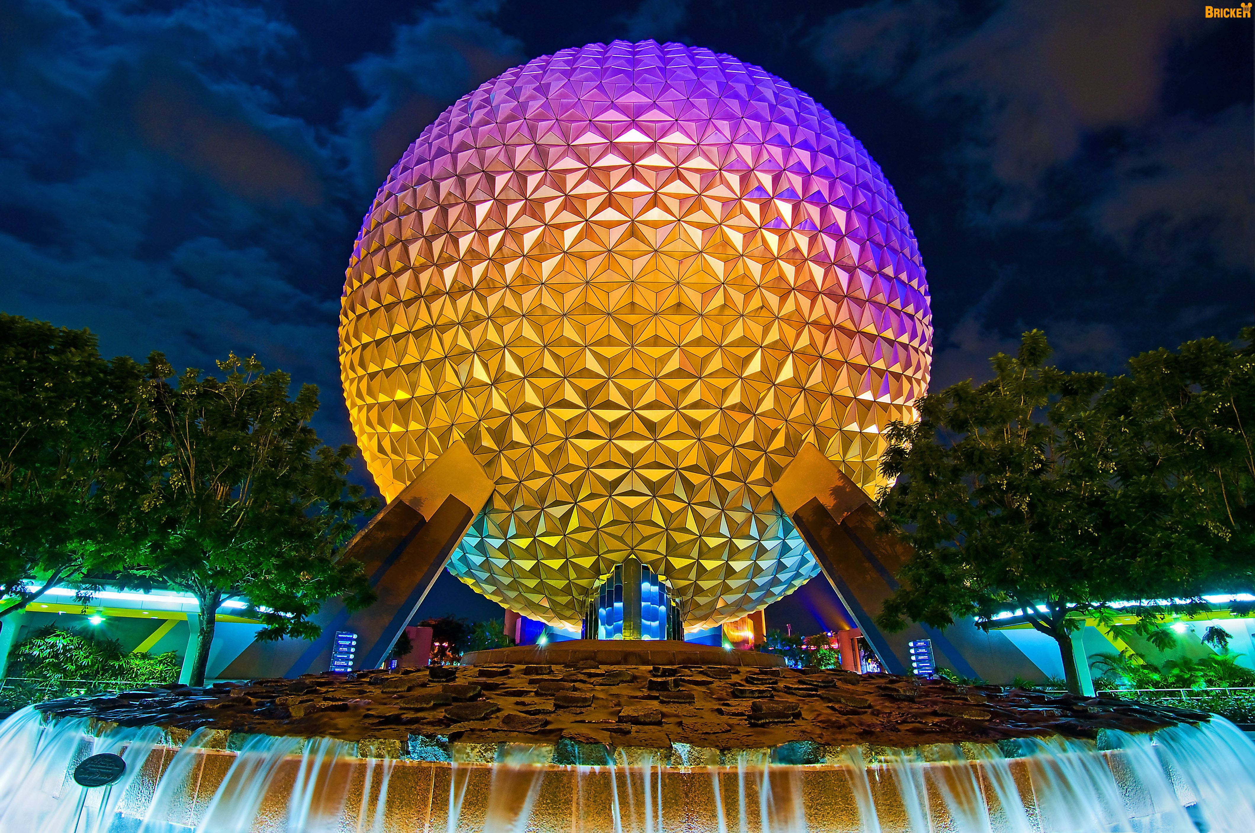 金紫相間的Epcot噴泉 壁紙 — 一個巨大的測地線球體在漆黑的夜空下散發著溫暖的黃色和紫色光芒，周圍環繞著樹木和下方層疊的噴泉。