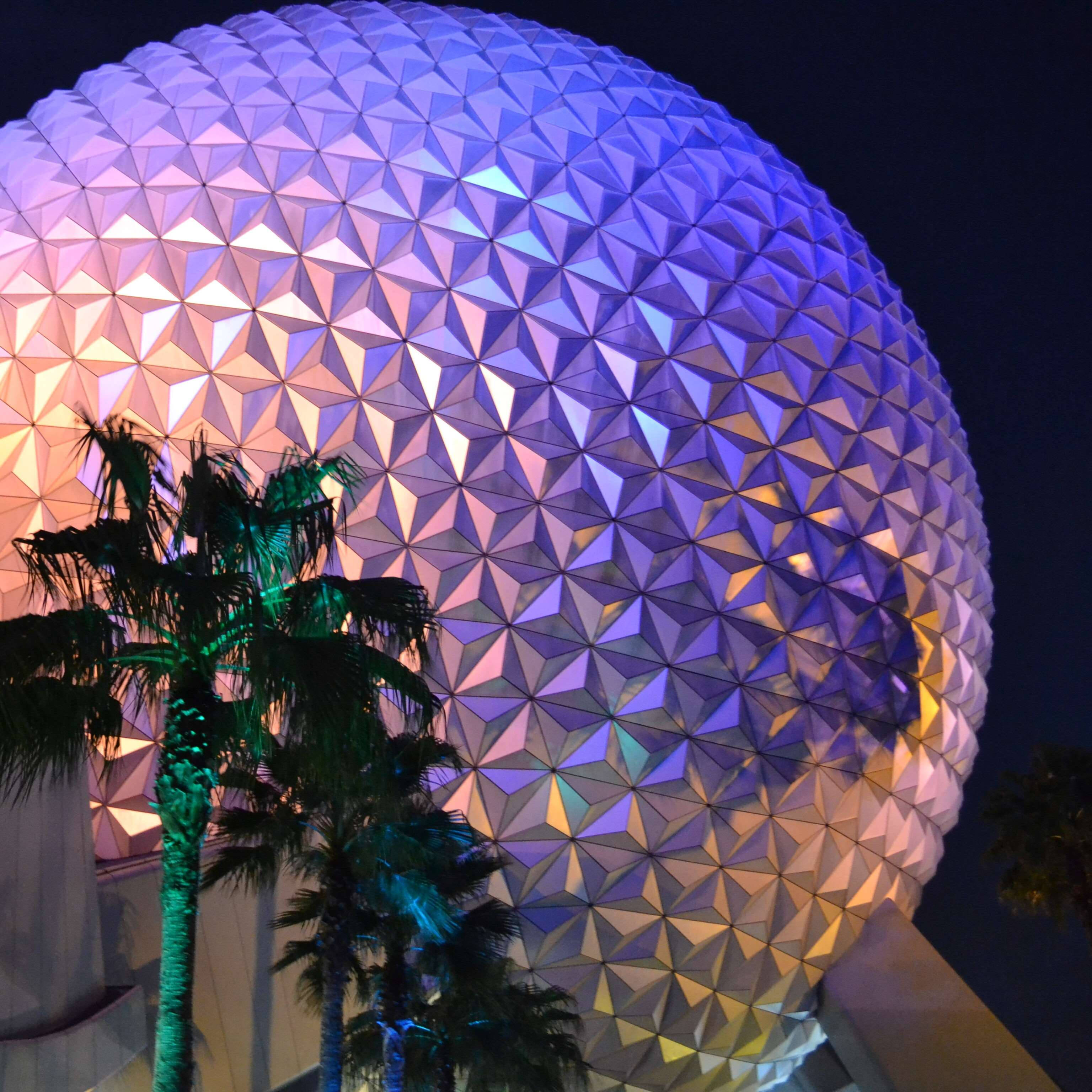 色彩繽紛的Epcot地球儀與樹木 壁紙 — 一個巨大的測地圓頂，以充滿活力的紫色和橙色燈光照亮，在黑暗的夜空下聳立在棕櫚樹的剪影之上。