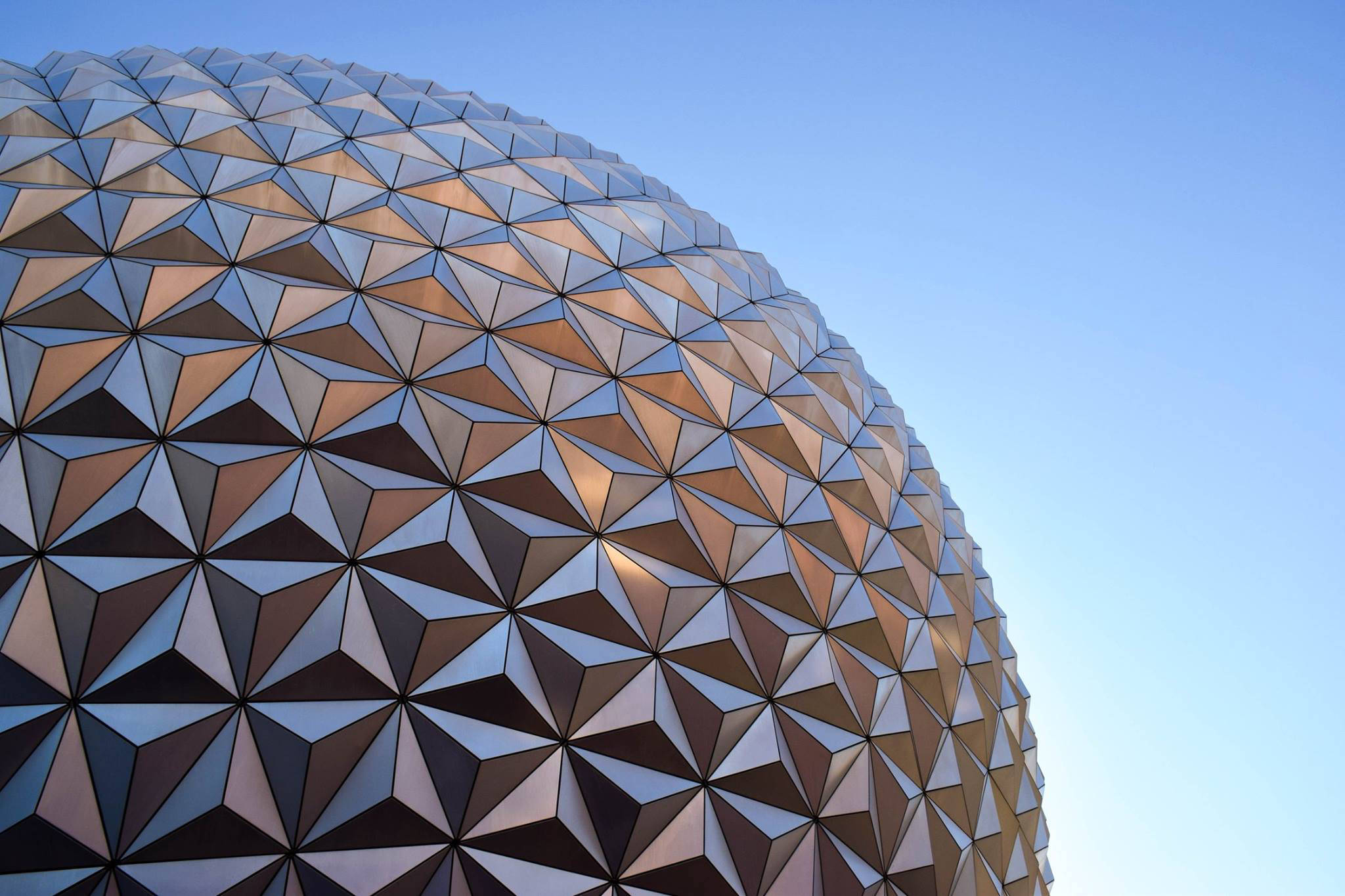 Epcot 球體特寫 壁紙 — 低角度觀看測地線穹頂的金屬三角形面，在清澈藍天下捕捉金色陽光。