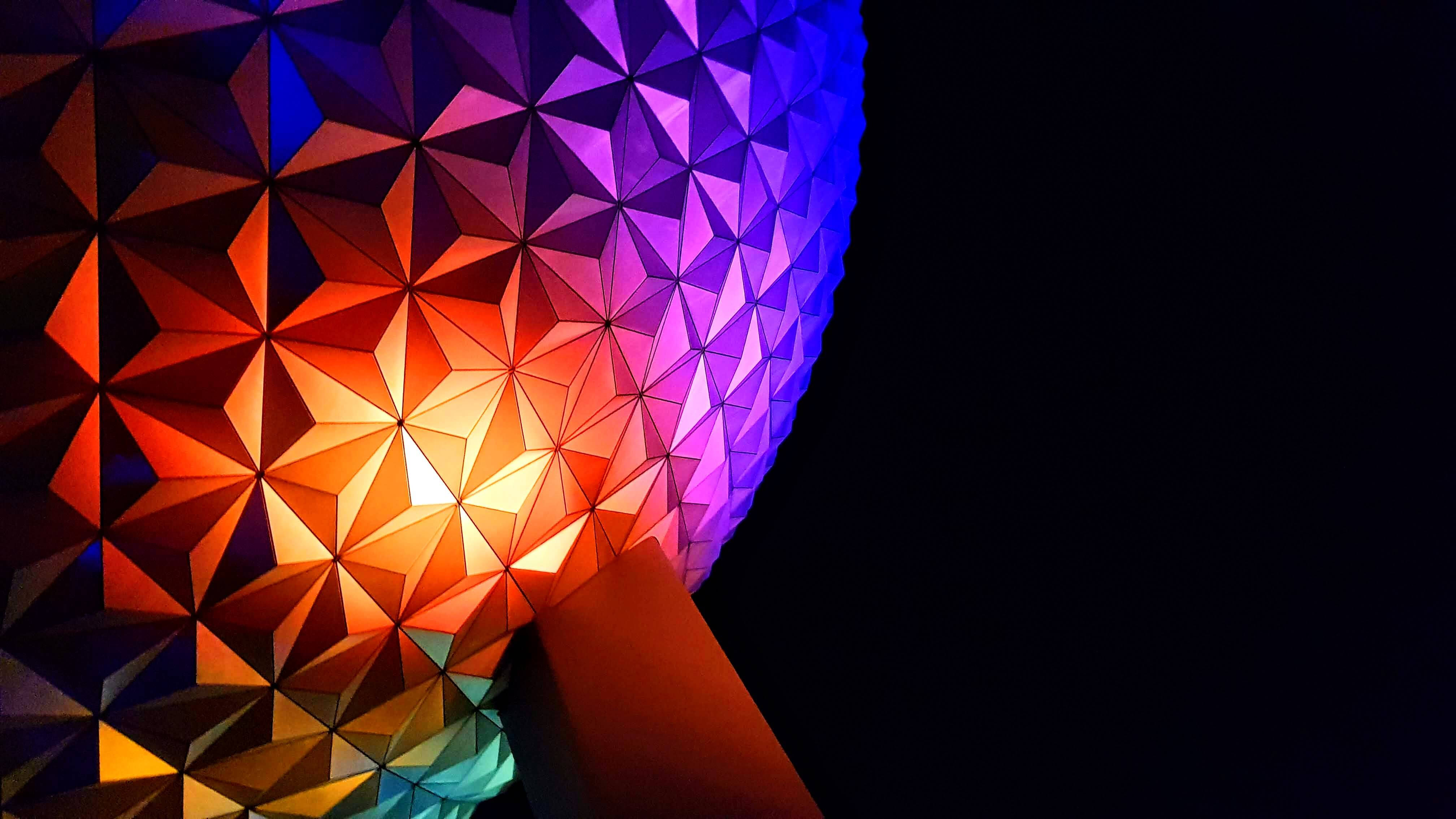 Epcot 球體立於支柱上 壁紙 — 一個充滿活力的幾何球體，帶有發光的橙色和紫色三角形切面，矗立在黑暗的夜空下。