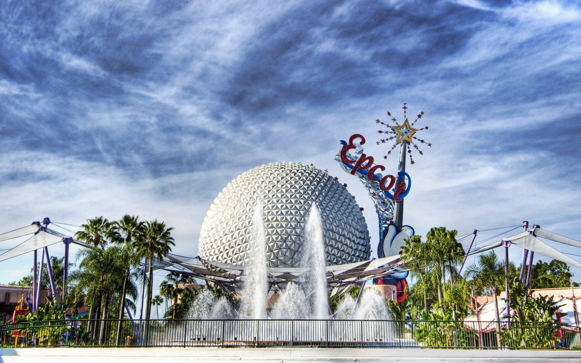 Epcot 球體與噴泉 壁紙 — 標誌性的 Epcot 球體在戲劇性的藍天下閃耀，噴泉在棕櫚樹和 Epcot 標誌前噴水。