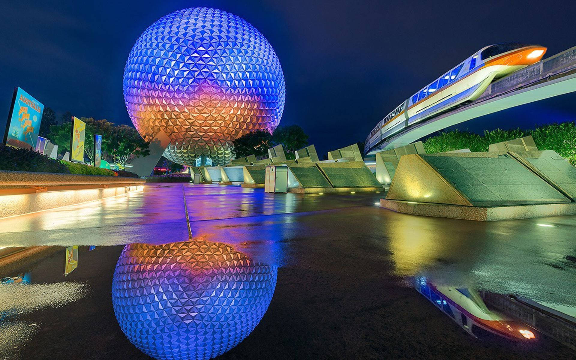 Epcot地球儀倒映於地面 壁紙 — 在Epcot，一個發光的測地線球體和單軌列車在漆黑的夜空下倒映在濕漉漉的路面上。