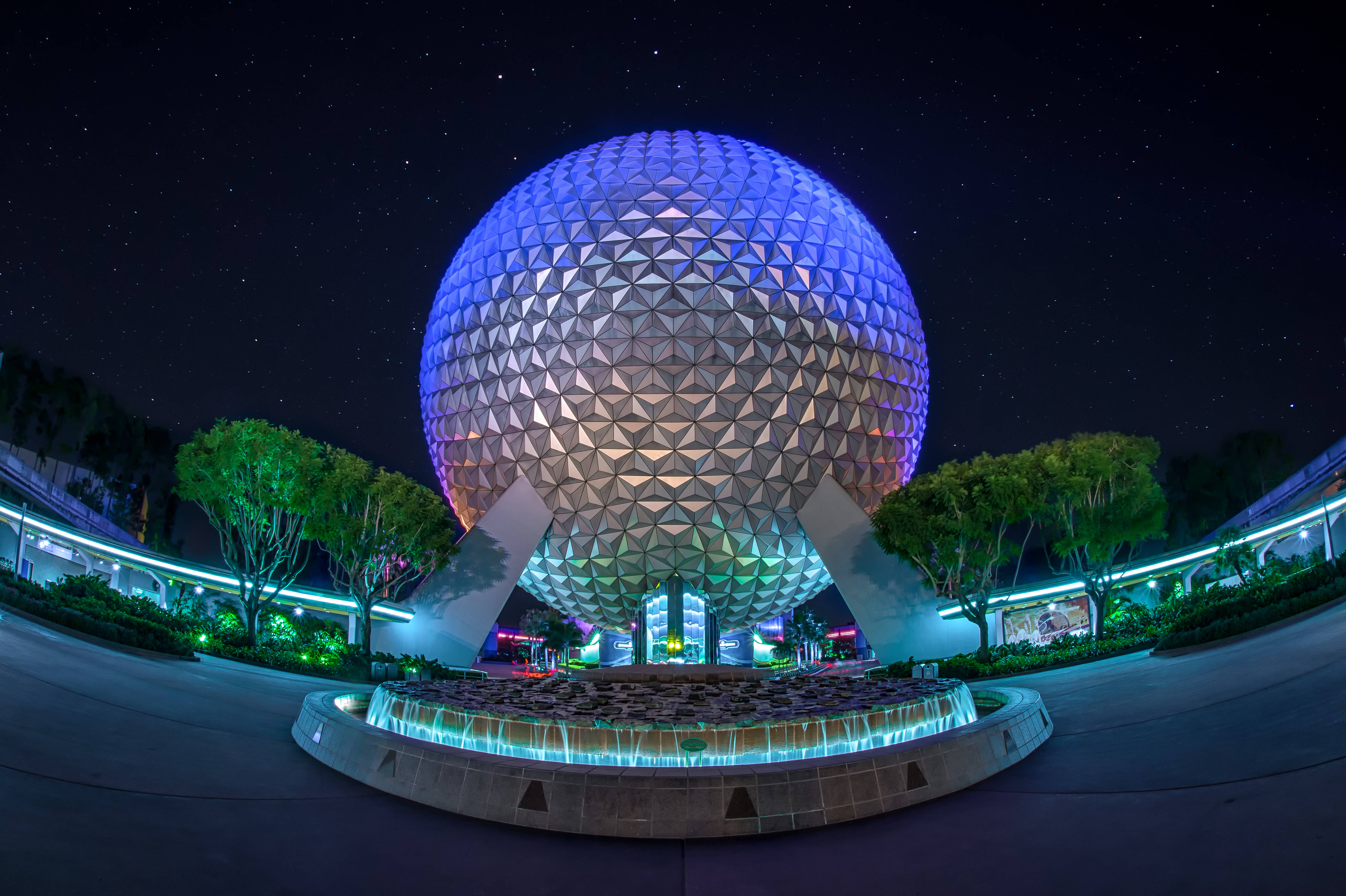 Epcot地球儀與繁星夜空 壁紙 — 一個巨大的發光測地線球體在圓形噴泉上方的星空夜空下發出藍色和紫色的光芒。