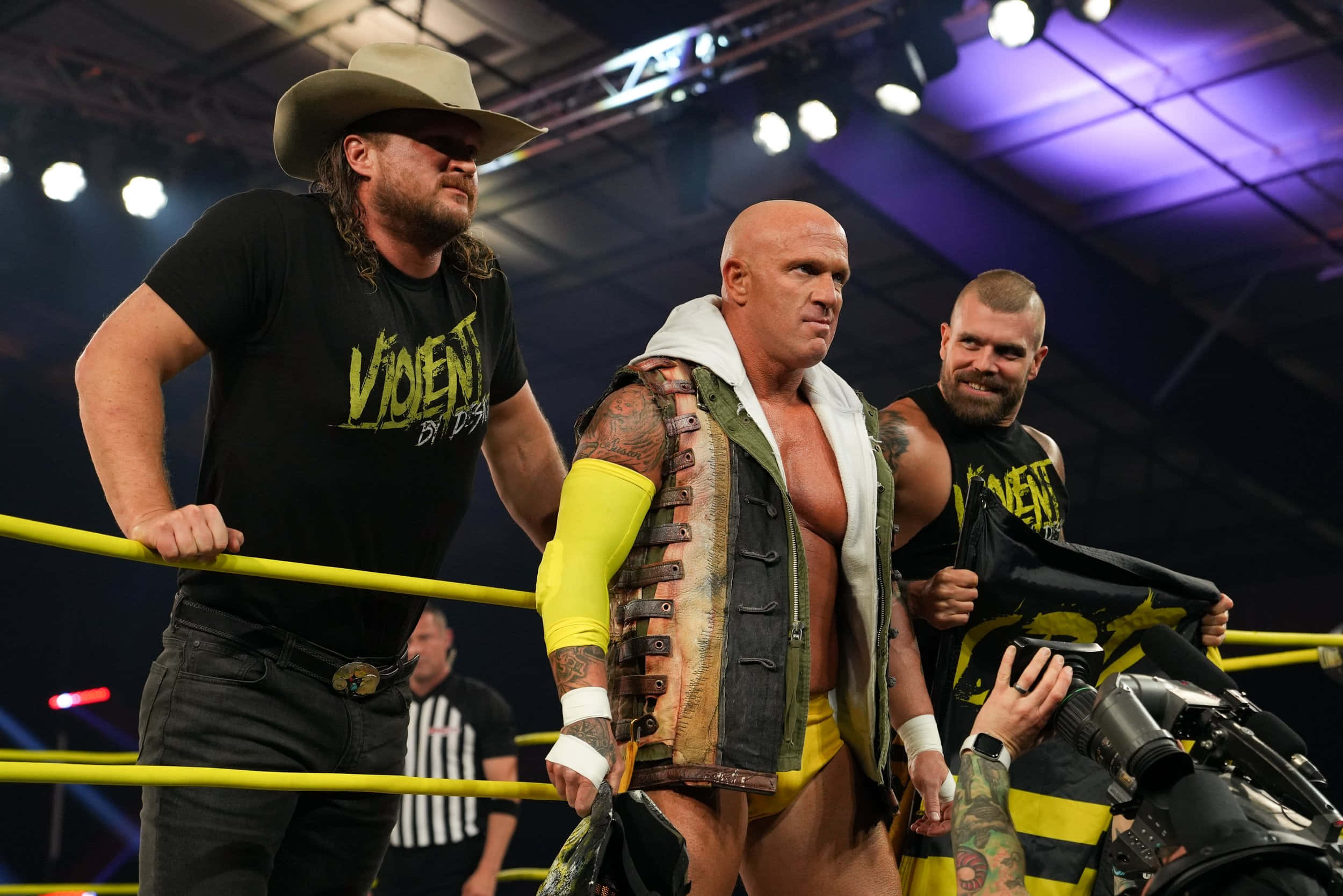 Eric Young 與 Joe 和 Cody 同框 壁紙 — 三名肌肉發達的摔角手在擂台上，其中一人戴著牛仔帽，另一人穿著皮背心，在明亮的場館燈光下。