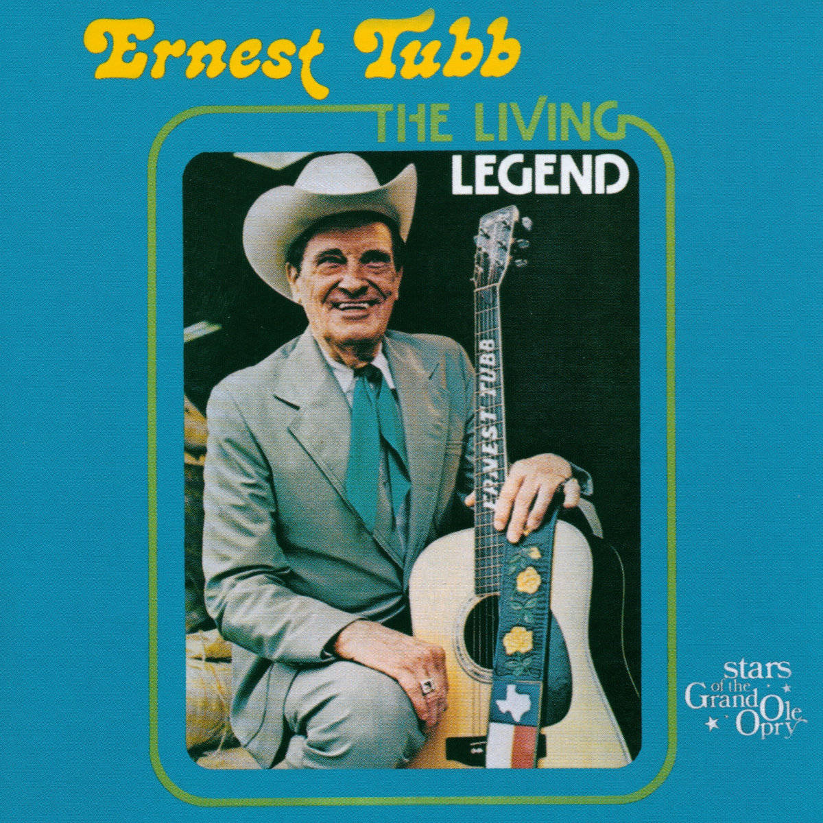 Ernest Tubb 在藍色背景上戴著牛仔帽拿著結他微笑