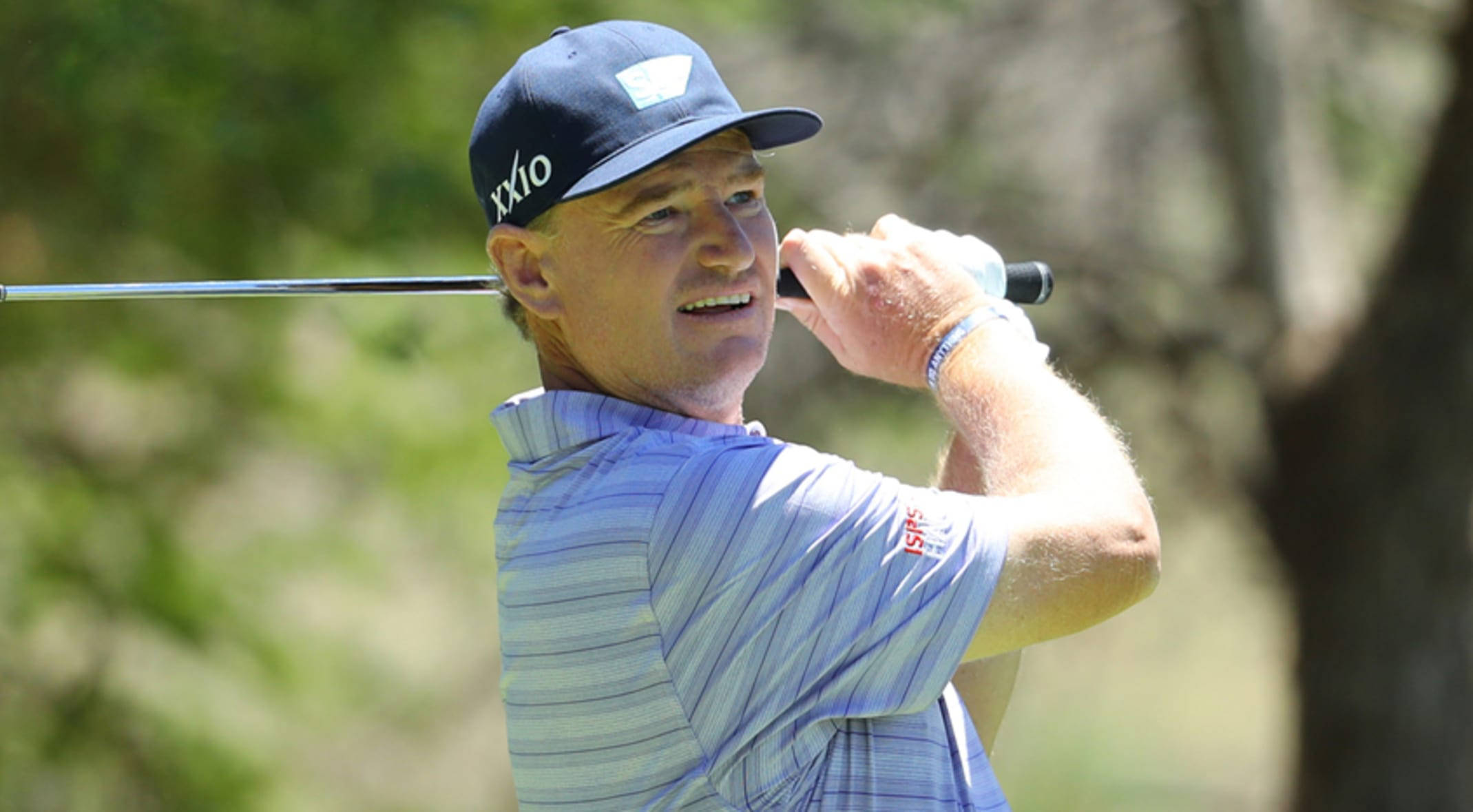 Ernie Els 高爾夫揮杆後微笑 壁紙 — 高爾夫球手在陽光普照、樹木成排的球道上專注揮桿。
