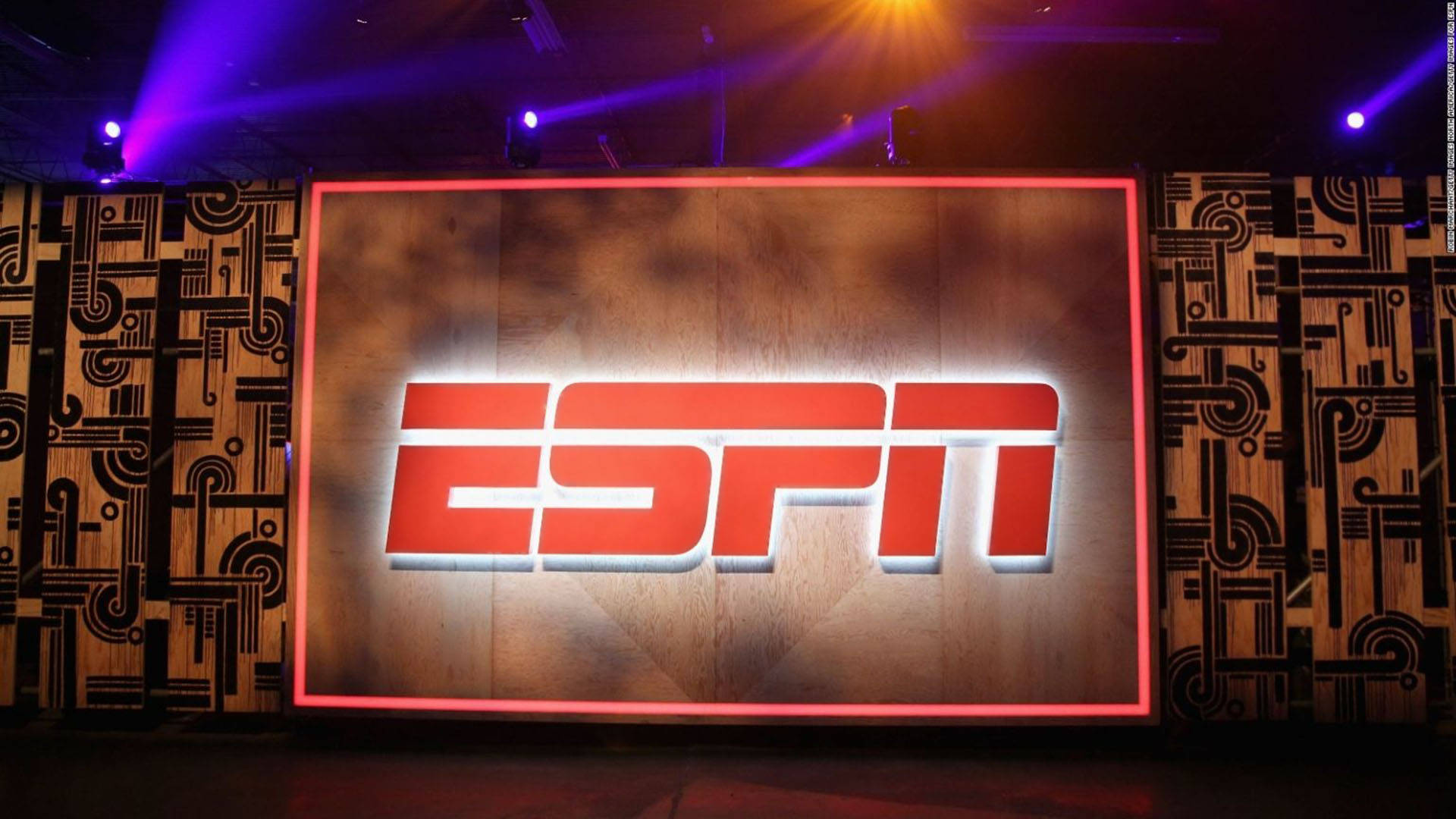 木質ESPN標誌壁紙 壁紙 — 一個大型發光的ESPN標誌在紫色舞台燈光下，在帶有圖案牆壁的木製屏幕上發出紅光。