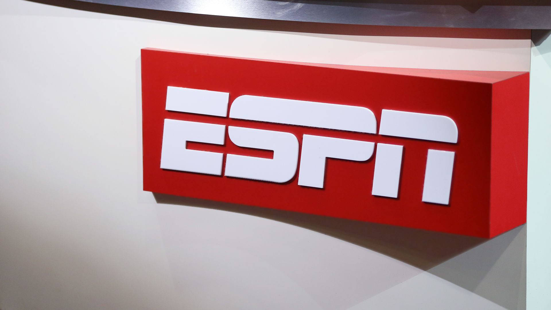 ESPN電視台標誌壁紙 壁紙 — 一個大膽的紅色ESPN標誌，帶有白色字體，安裝在潔白的牆壁上，投射出柔和的陰影。
