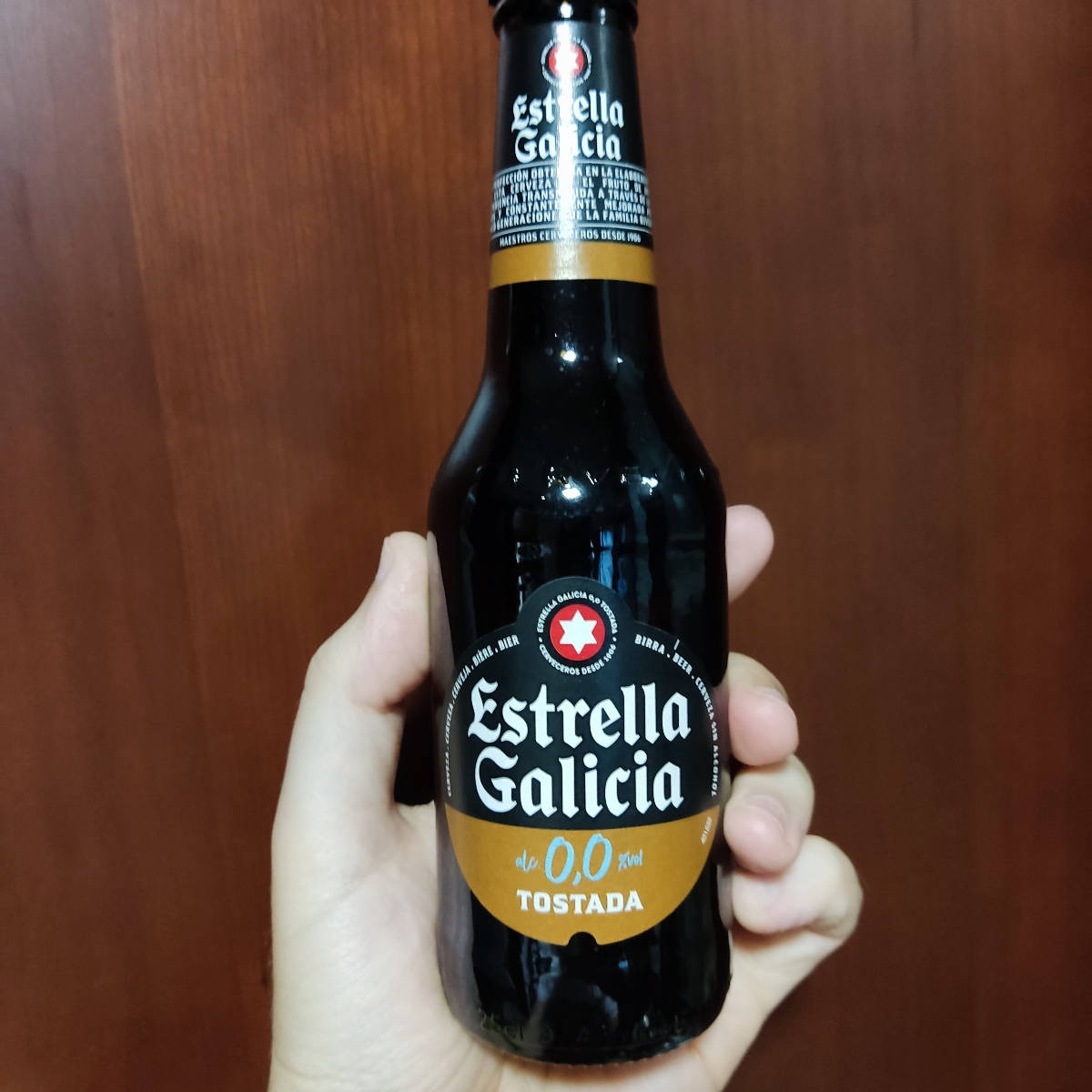 手拿Estrella Galicia 0,0 Tostada啤酒瓶靠在木頭上。