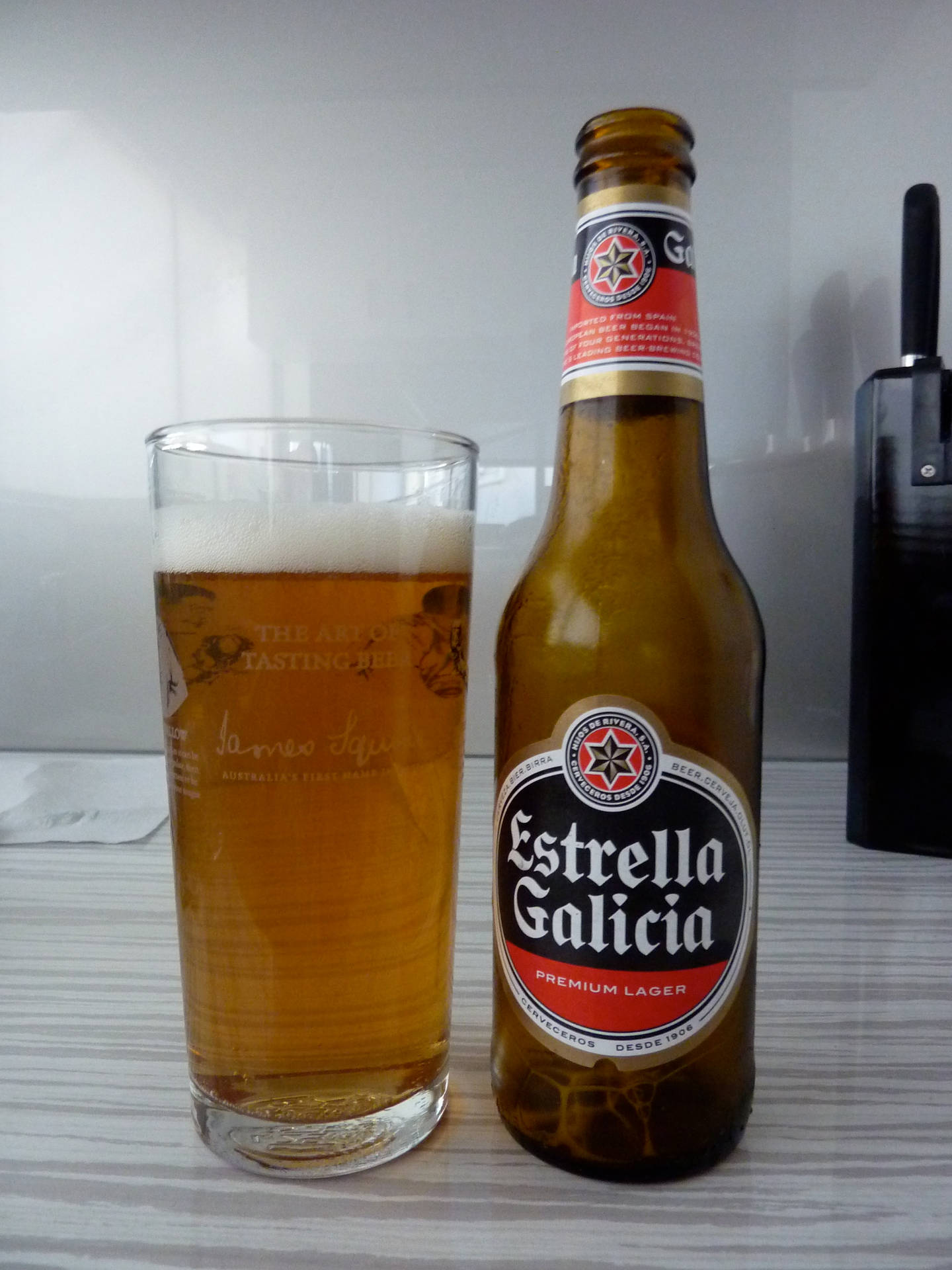 木桌上的一瓶和一杯Estrella Galicia啤酒。