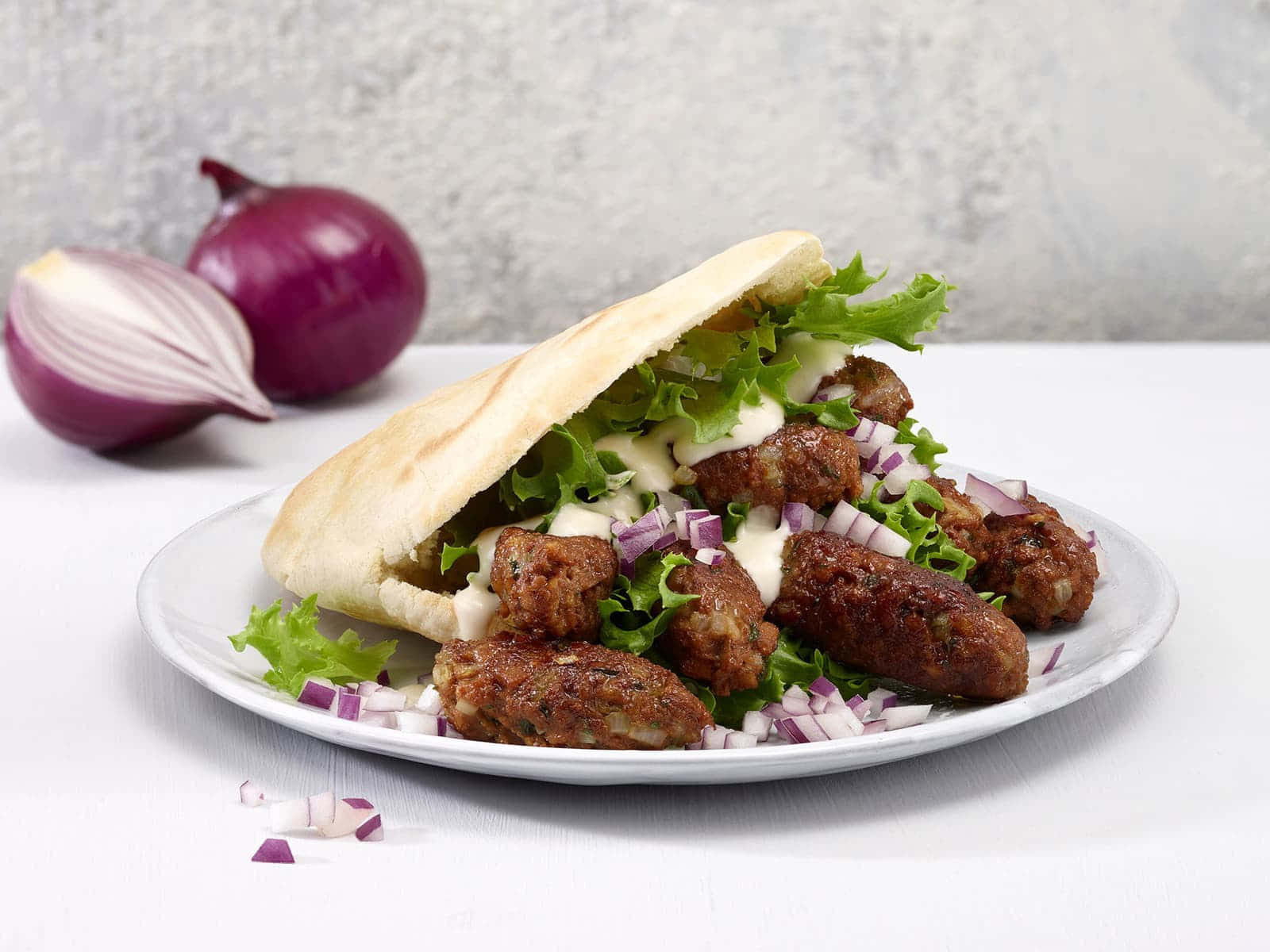 Ćevapi香腸沙拉 壁紙 — 新鮮製作的中東炸豆丸子三文治，配上香脆肉丸、生菜和紅洋蔥，放在白色碟上，背景有原個洋蔥。