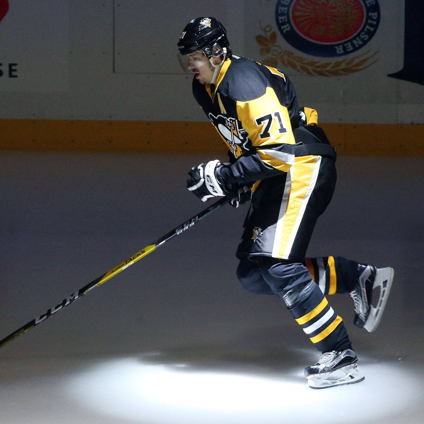 Evgeni Malkin 匹茲堡企鵝隊聚光燈下 壁紙 — 一名身穿黑色和黃色裝備的曲棍球運動員在明亮的場館燈光下在冰上激烈滑行。