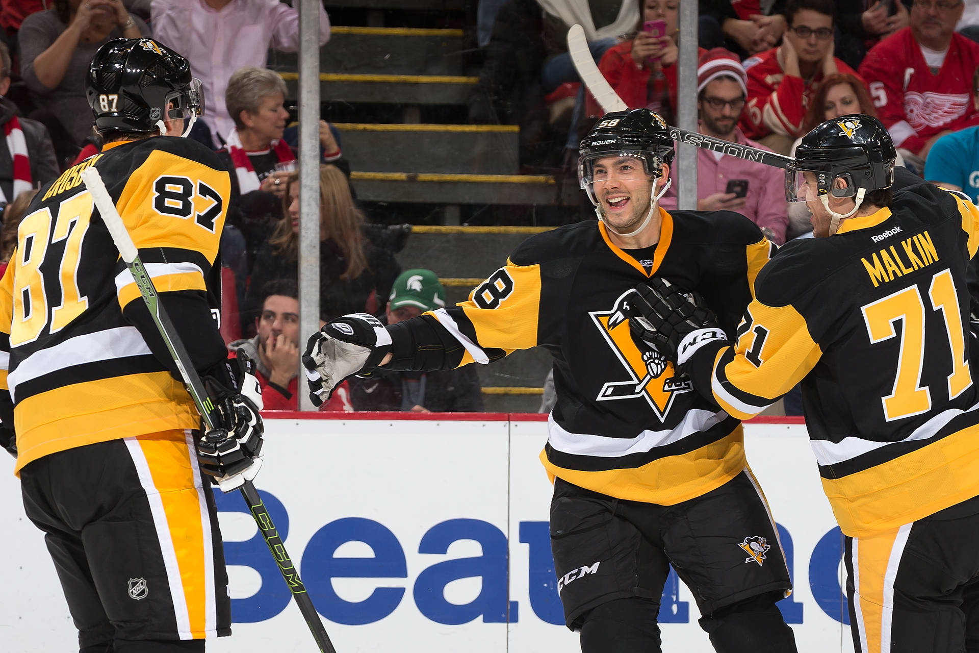 Evgeni Malkin 匹茲堡企鵝隊隊友歡笑 壁紙 — 三名身穿黑色和金色球衣的匹茲堡企鵝冰球運動員在冰上慶祝入球，背景有球迷。