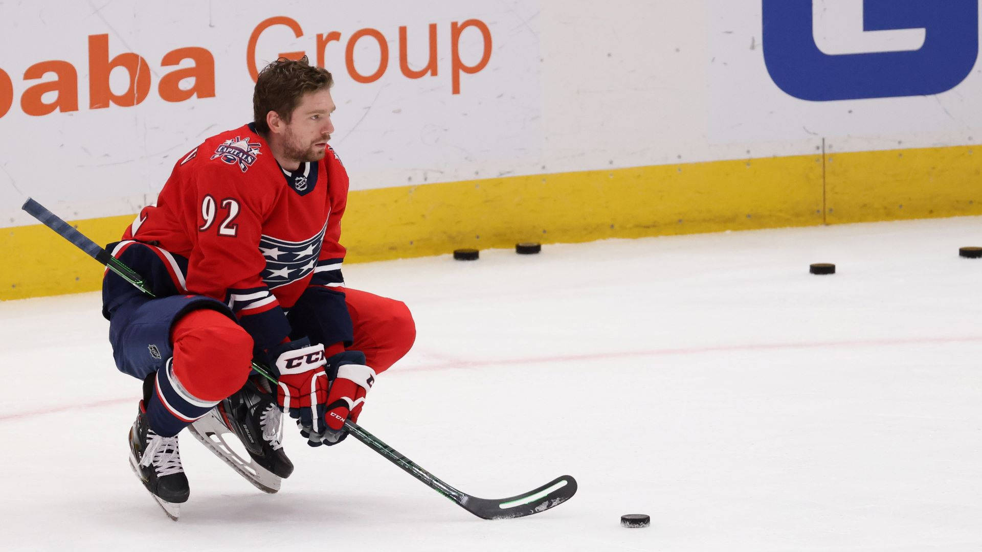Evgeny Kuznetsov 冰上精彩攻防 壁紙 — 一名身穿紅色球衣92號的冰球運動員在冰上低蹲，專注地將球桿靠近冰球。