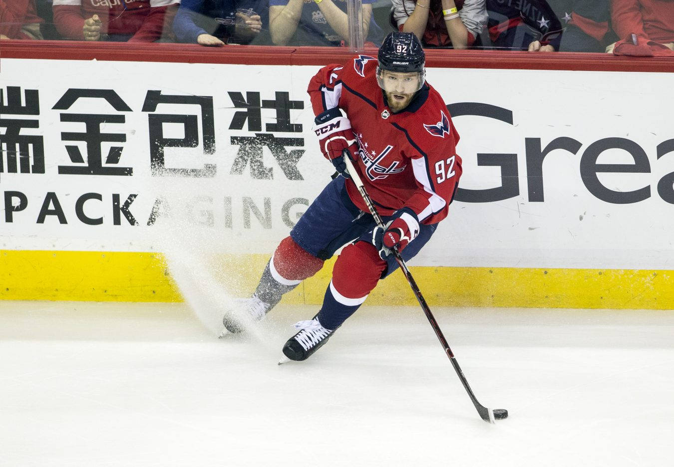 Evgeny Kuznetsov 即將得分 壁紙 — 一名身穿紅藍球衣的冰球運動員在比賽中帶著冰球和球桿在冰上激烈滑行。