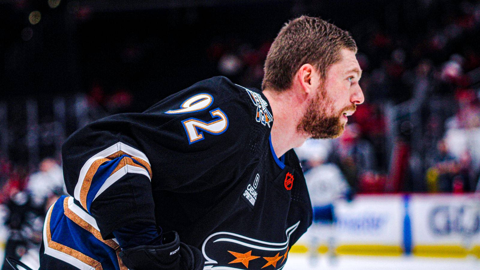 Evgeny Kuznetsov 穿著時尚黑色戰衣 壁紙 — 一名專注的冰球運動員身穿黑色22號球衣，在明亮的場館燈光下於冰上向前傾身比賽。