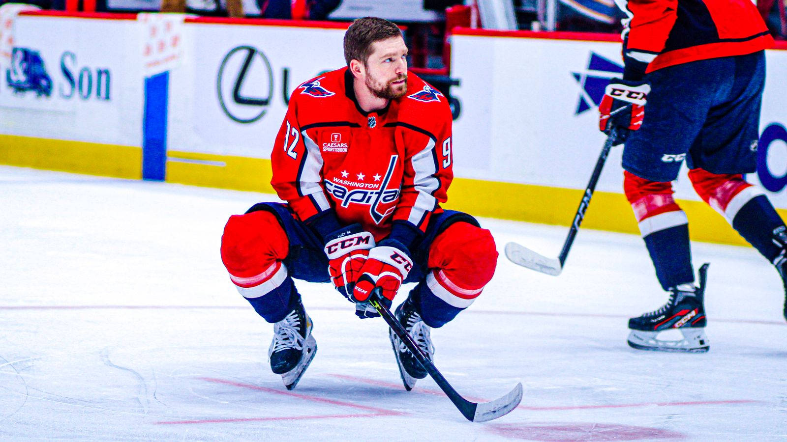 Evgeny Kuznetsov 冰場風采 壁紙 — 一名穿著紅色華盛頓首都隊球衣的冰球運動員在比賽中低蹲在冰上，手持球桿。