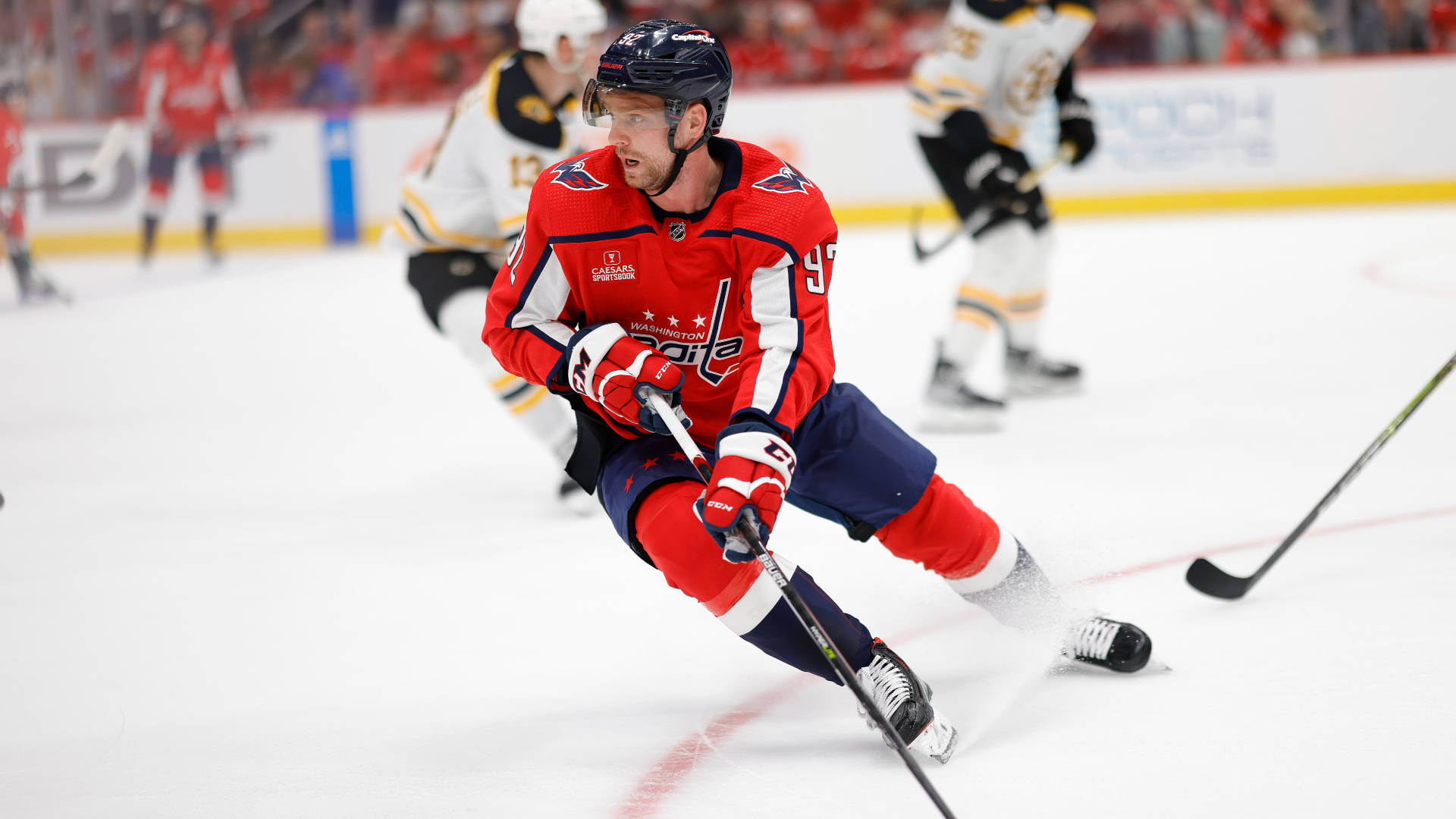 Evgeny Kuznetsov 擊球制勝 壁紙 — 一名身穿紅色球衣的曲棍球運動員在快速比賽中，在冰上傾身進行急轉彎，專注力極高。