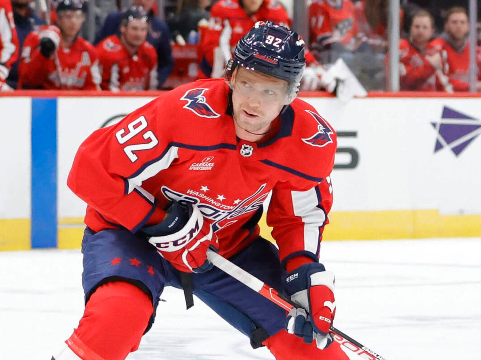 Evgeny Kuznetsov 準備射門 壁紙 — 一名穿著紅色華盛頓首都隊球衣的冰球運動員在比賽中蹲低在冰上，手持球桿。