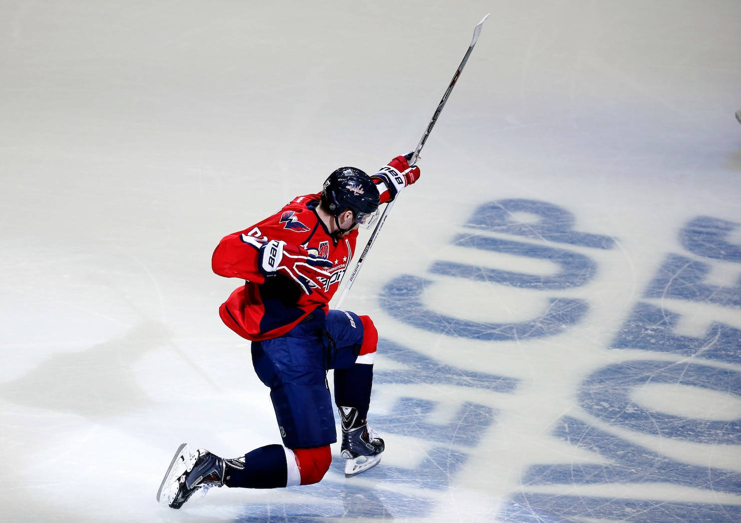 Evgeny Kuznetsov 成功進攻 壁紙 — 一名身穿紅藍球衣的冰球運動員在入球後跪在冰上，高舉球棍慶祝勝利。