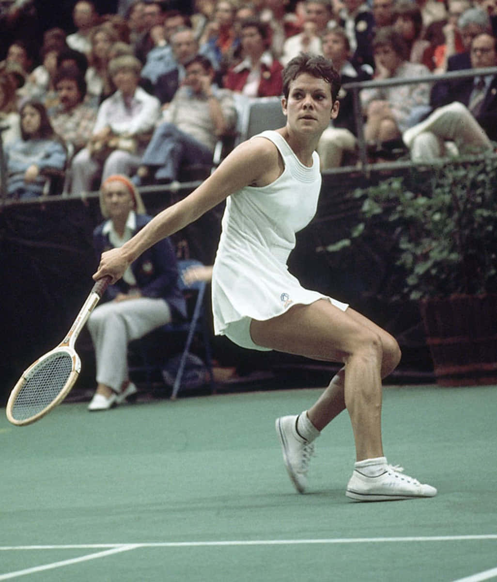 Evonne Goolagong Cawley 1976年 Virginia Slims 預賽 壁紙 — 一位身穿白色運動服的女網球手在綠色球場上向前衝刺，背景有觀眾。