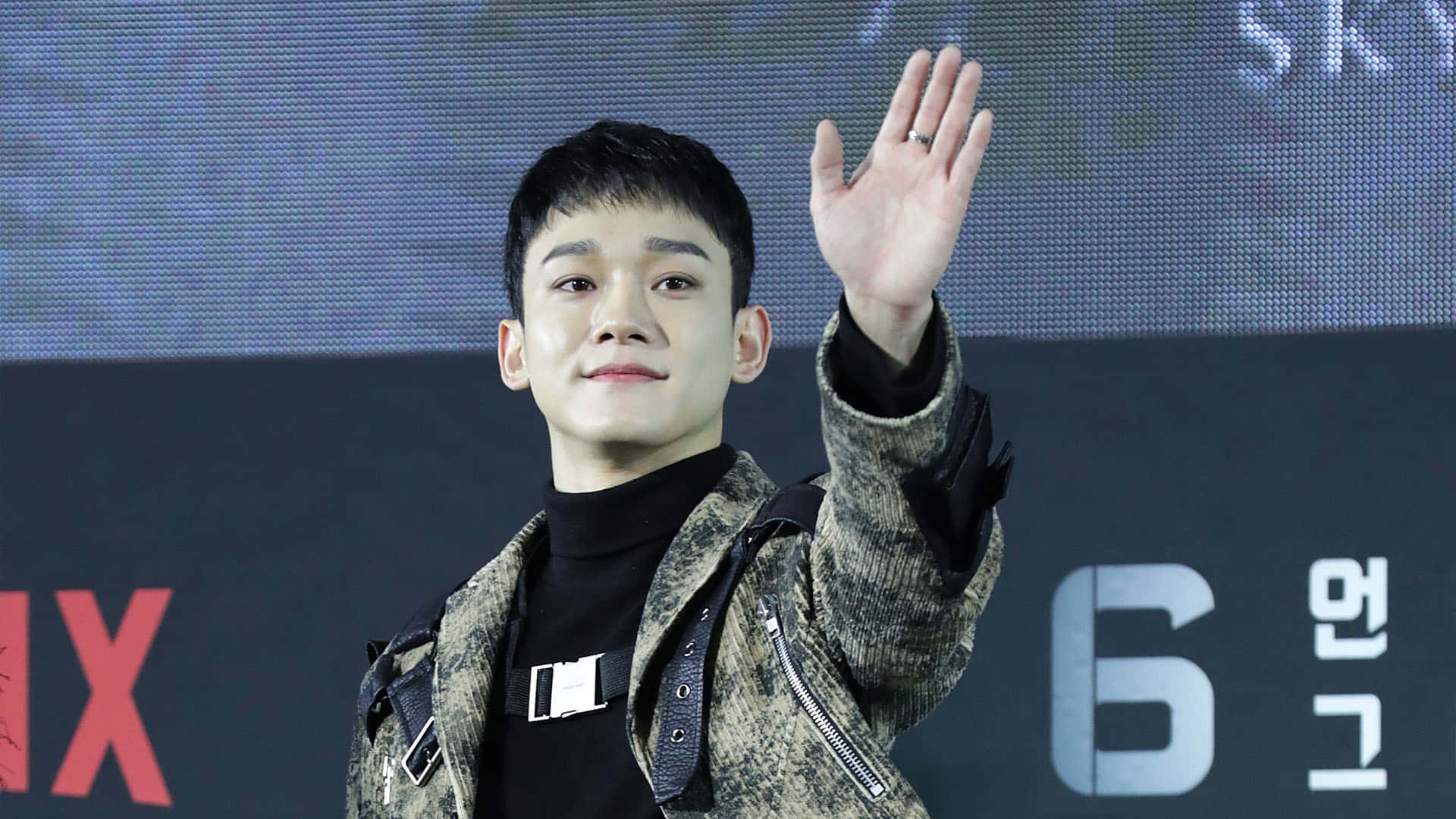 EXO 成員拍攝寫真 壁紙 — 一位身穿圖案外套的年輕人在Netflix活動背景前開心地揮手。