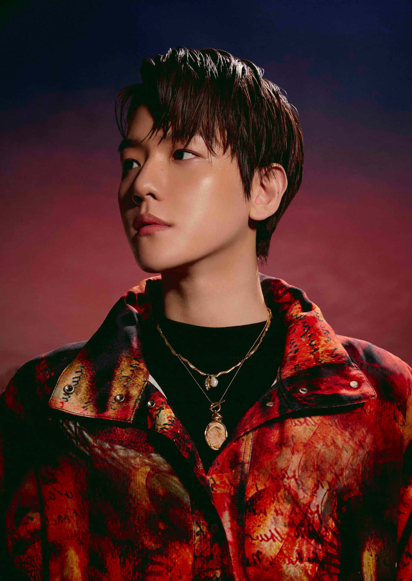 EXO現場演出震撼畫面 壁紙 — 一位年輕男子梳著深色時尚髮型，穿著鮮豔的紅色圖案外套，背景是帶有氛圍感的紫色和紅色漸變色。