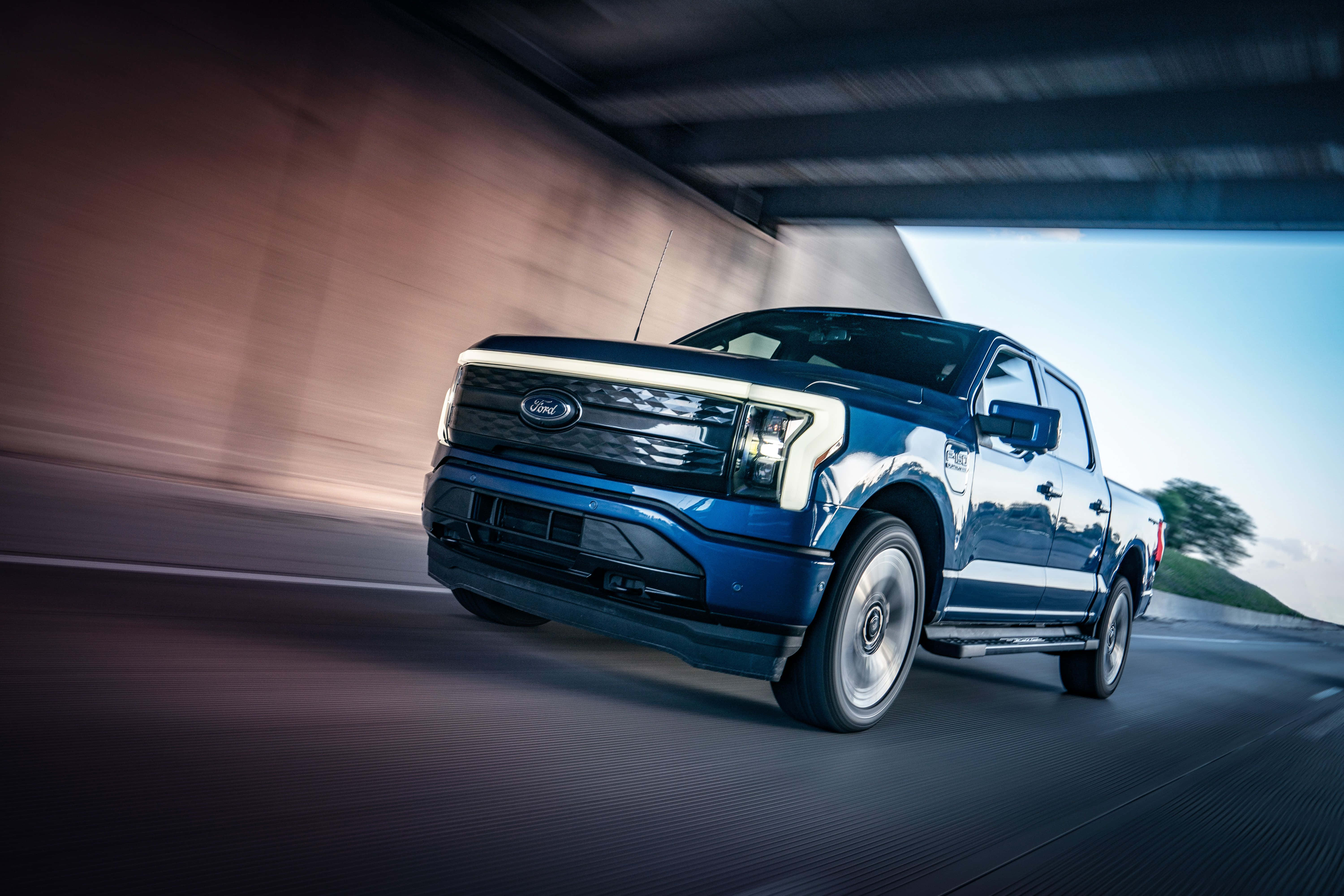 福特F-150電動版動態駕馭 壁紙 — 一輛時尚的藍色福特電動皮卡在混凝土天橋下高速行駛，道路上帶有動態模糊效果。