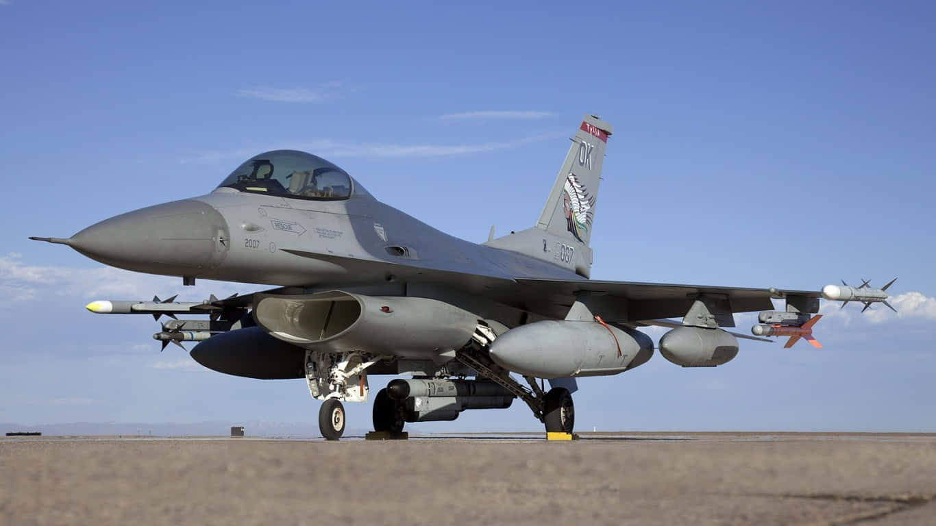 F-16 機群停泊於跑道的巨型客機背景（1366x768） 壁紙 — 一架灰色F16戰鬥機配備導彈，停在停機坪上，天空湛藍清澈。