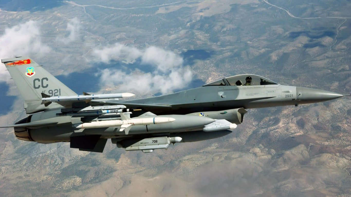 F-16 飛越地面的巨型客機背景（1366x768） 壁紙 — 一架灰色戰鬥機在崎嶇的山地上空翱翔，下方有零星雲層。