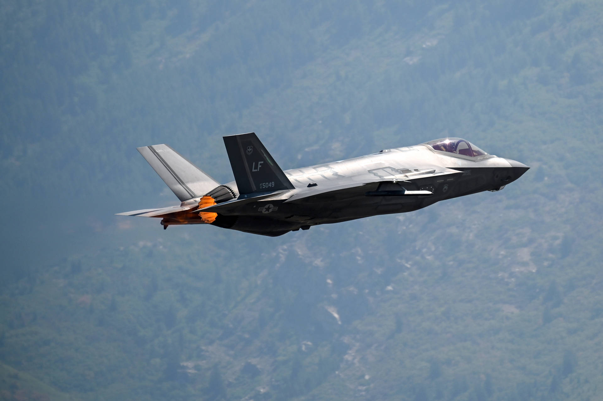 F-35戰鬥機在森林覆蓋的山脈上空飛行，後燃器啟動。
