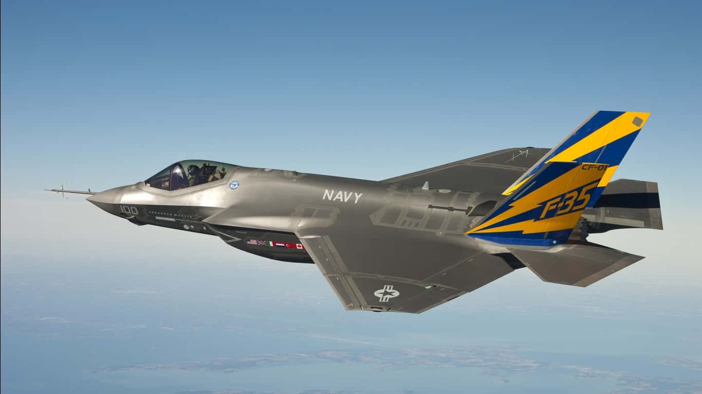 F-35C 在晴空飛行的巨型客機背景（1366x768） 壁紙 — 一架帶有藍黃色尾翼標誌的時尚灰色F35戰鬥機在遠處雲層之上的清澈藍天中翱翔。