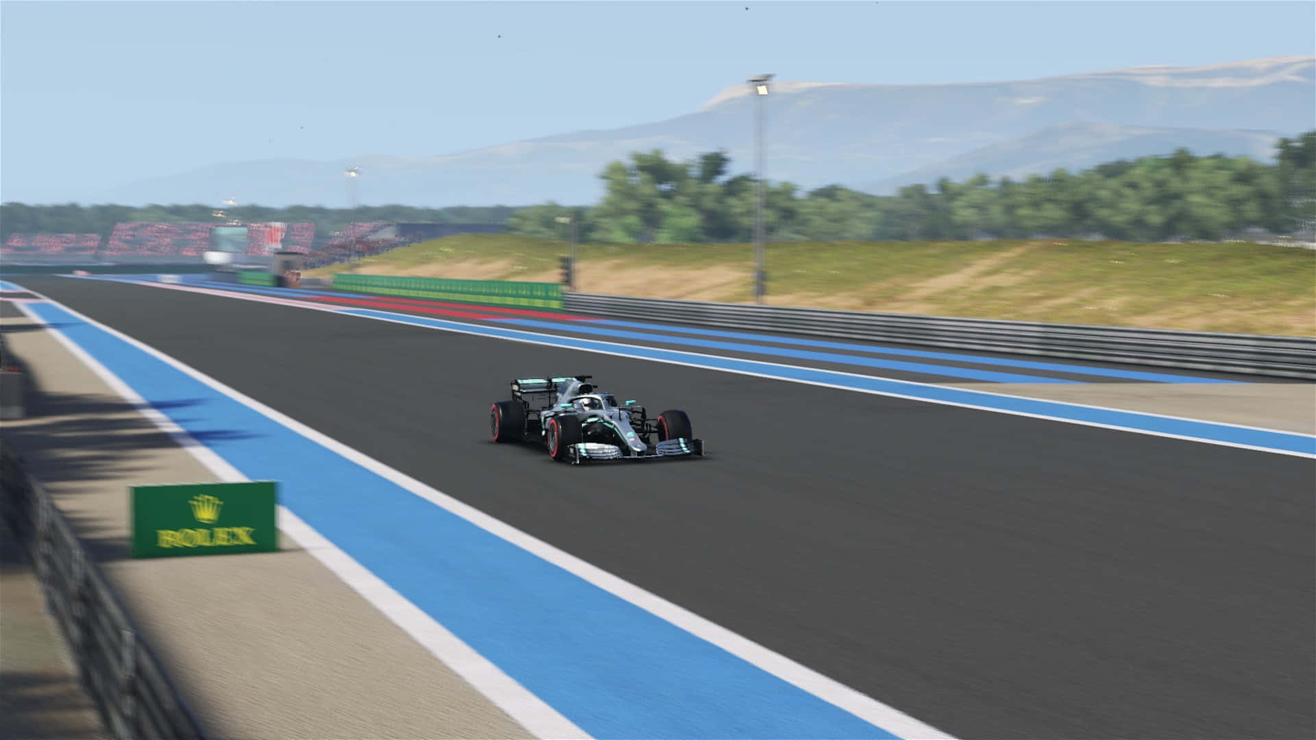 F1 2019賽道高清背景 壁紙 — 一架流線型銀色一級方程式賽車在陽光普照的賽道上奔馳，賽道有藍色路緣，遠處有綠色山丘，天空晴朗。