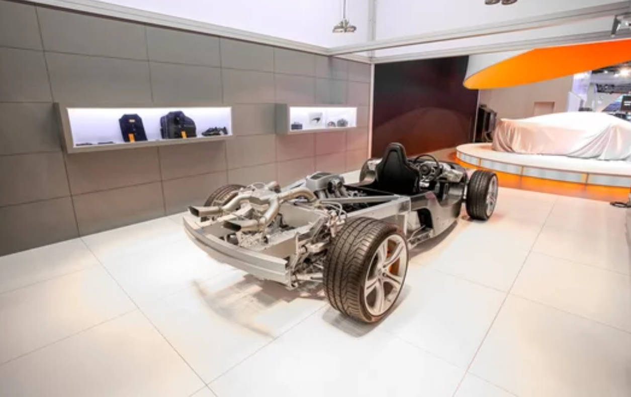在現代展廳中展示的銀色賽車底盤，帶有橙色點綴。