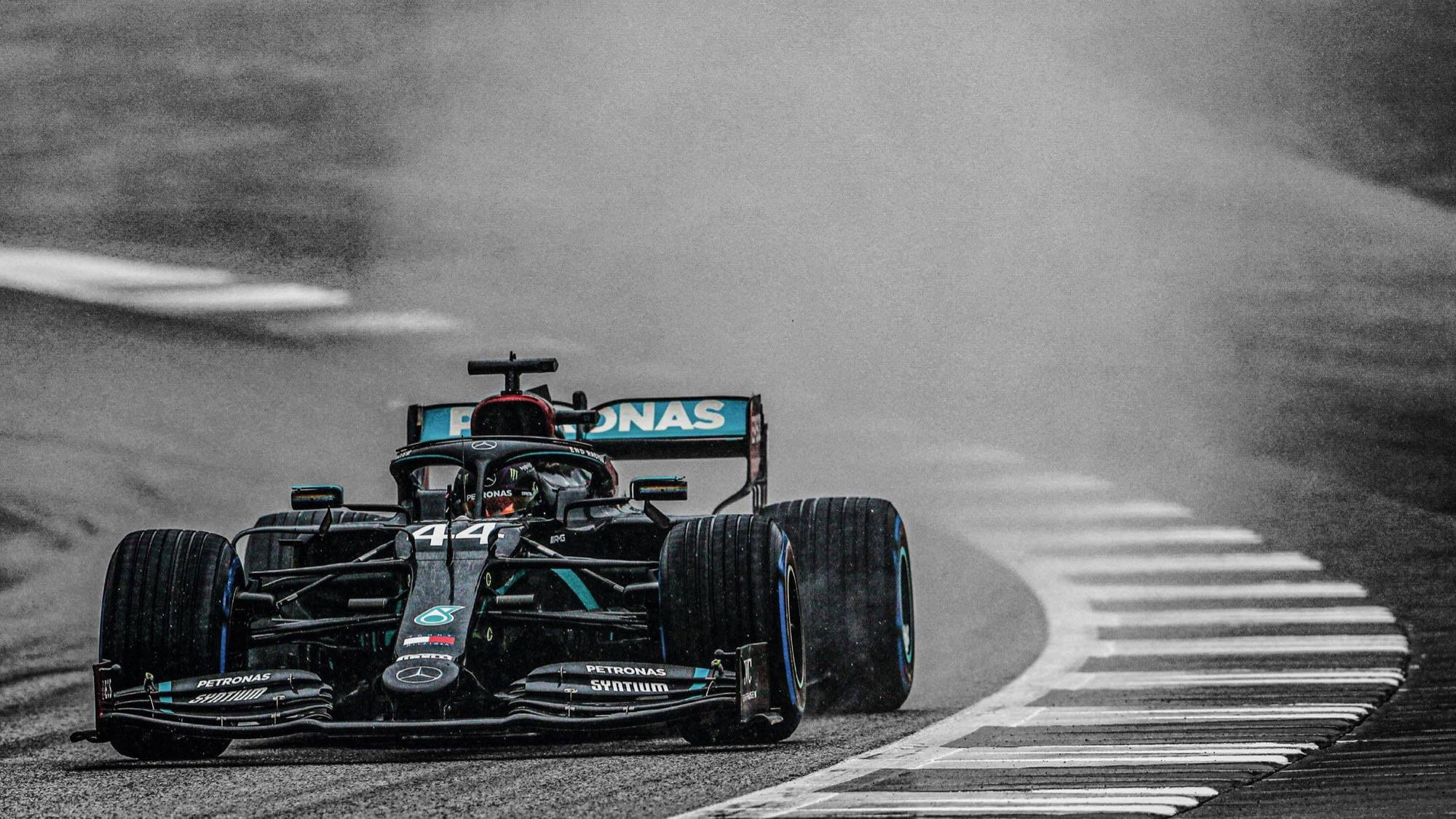 F1 Petronas AMG賽道疾馳 壁紙 — 一輛黑色和藍綠色的44號一級方程式賽車在賽道的濕滑彎道上疾馳，輪胎噴出水霧。
