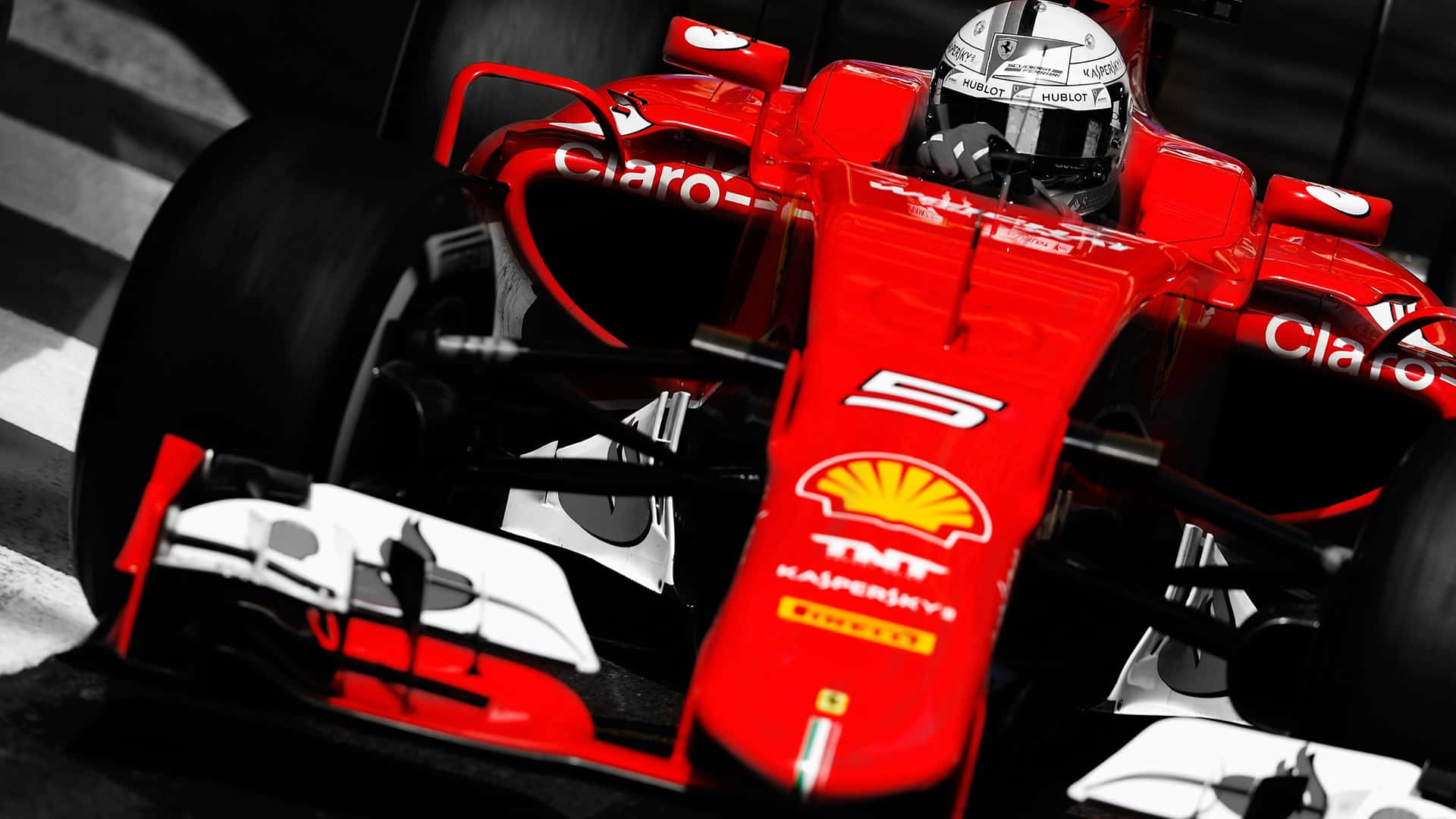 法拉利 F1 賽車疾馳賽道 壁紙 — 一架鮮紅色的F1賽車，車手戴著頭盔，在高對比度的黑白背景中衝過終點線。
